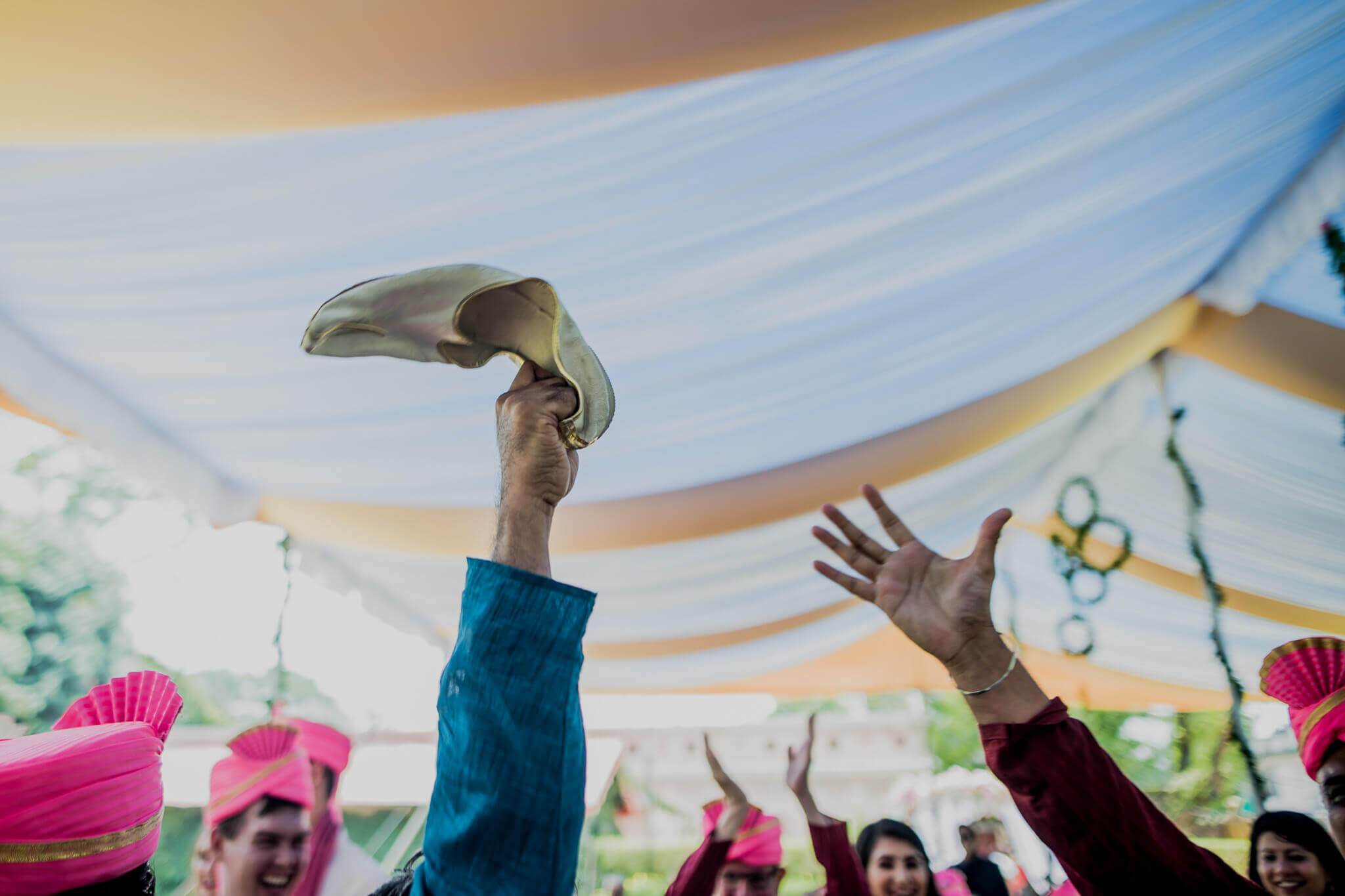 Groom Raghu raises his shoe triumphantly under colorful fabric canopy during celebration in Nepal