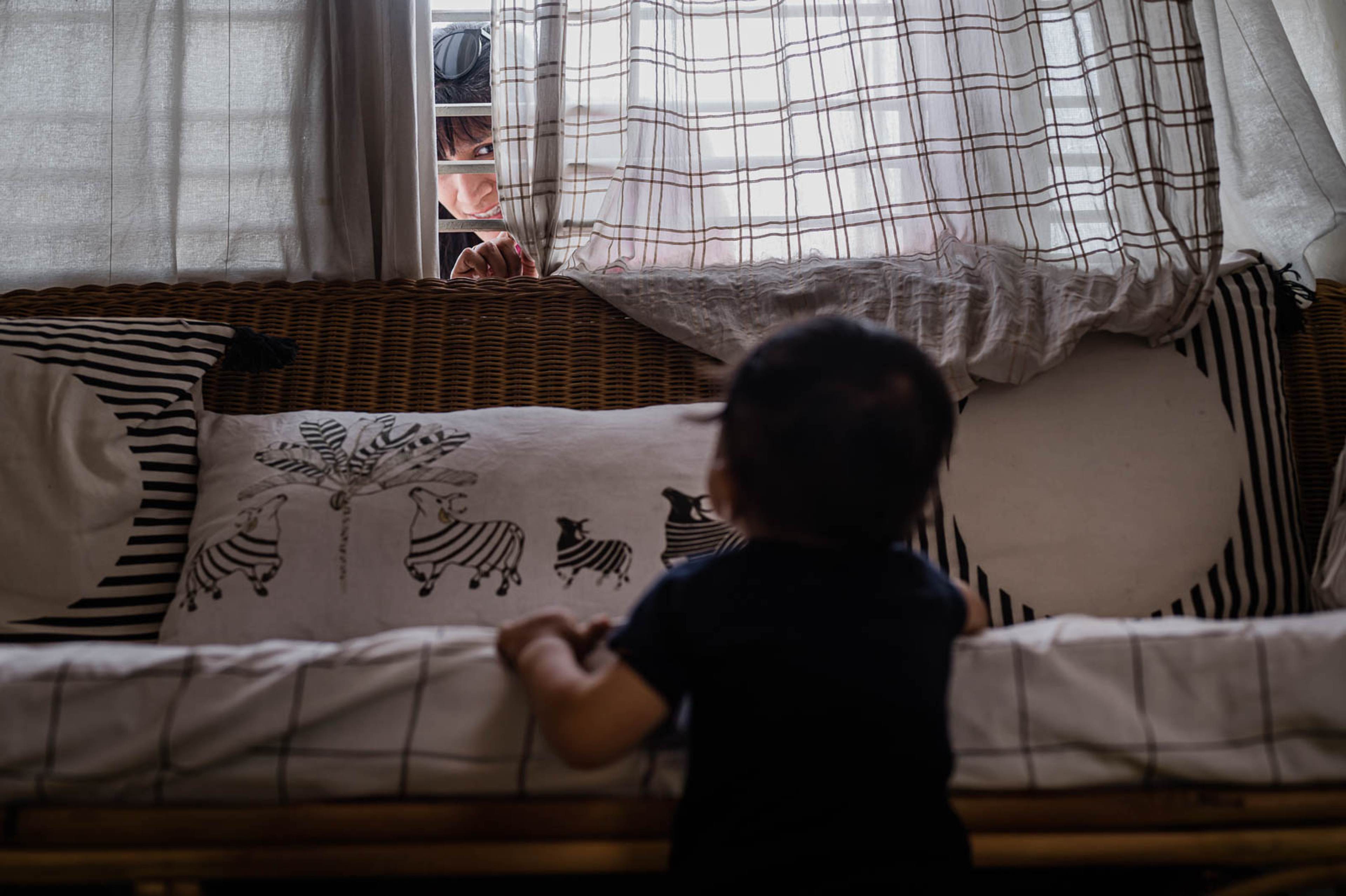 Child in dark clothing viewed from above on bed with patterned pillows and sheer canopy