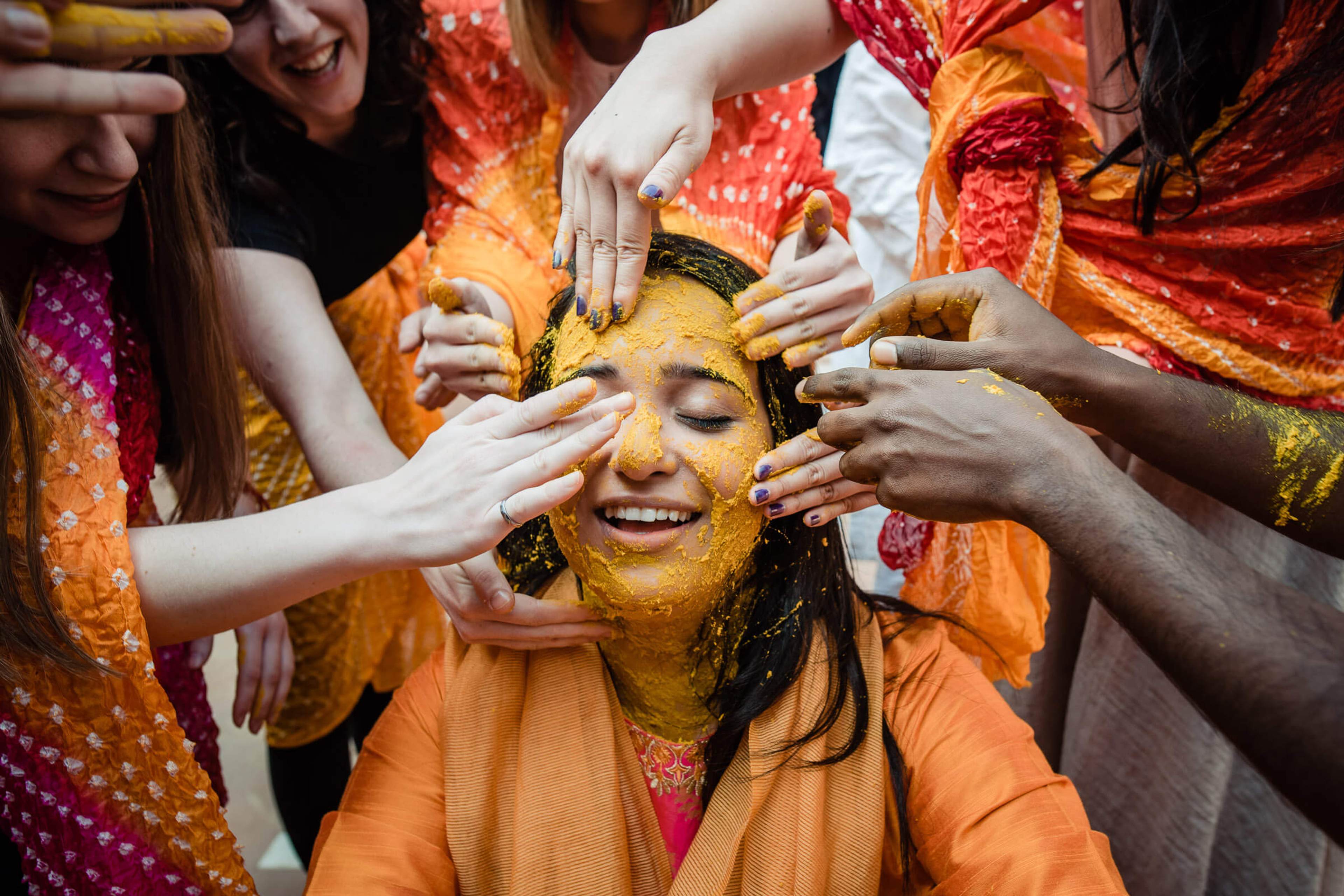 Maitrayee covered in golden turmeric paste, surrounded by laughing friends applying holi colors in Rajasthan