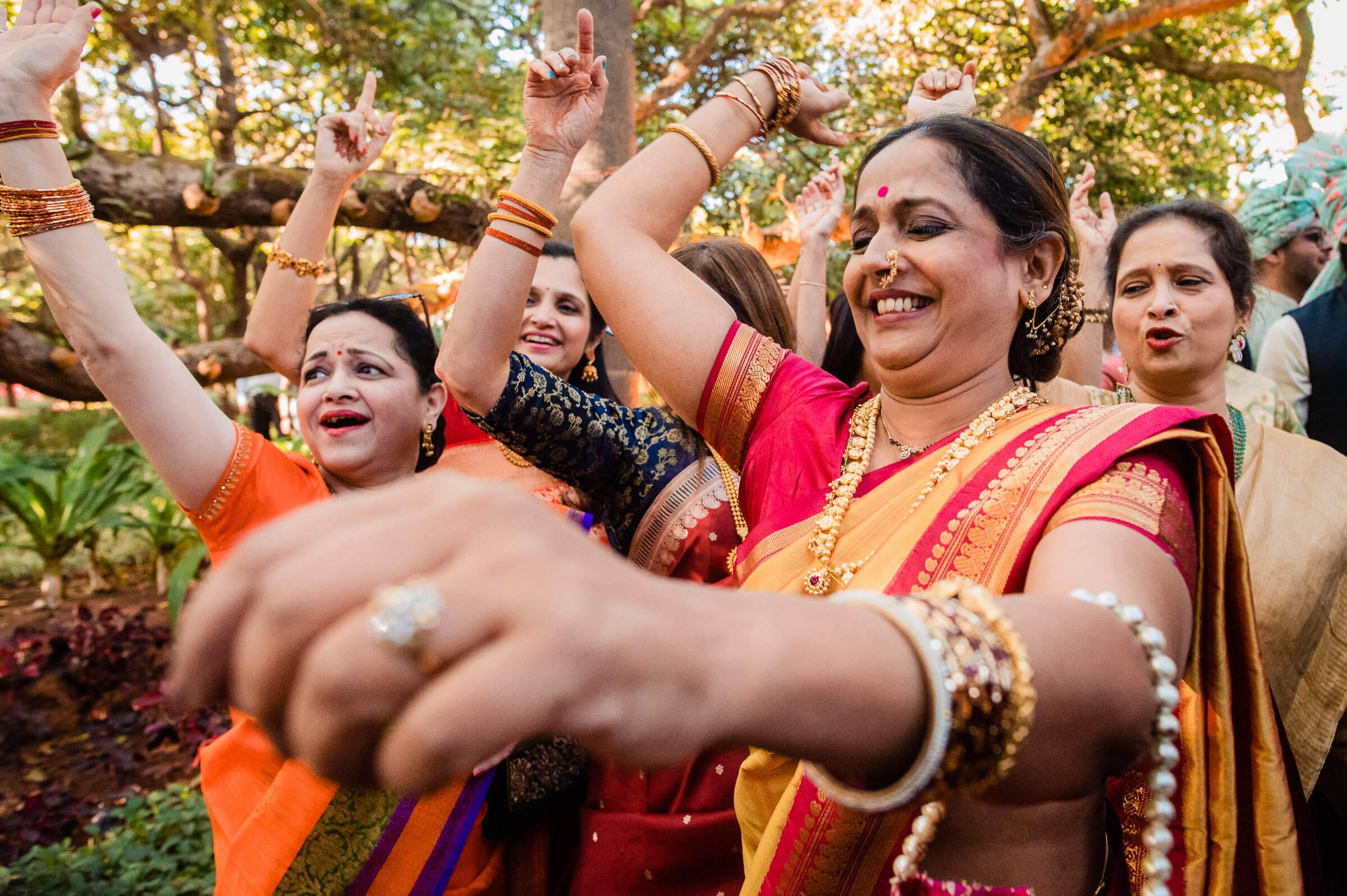 Women in colorful traditional Indian attire celebrating with raised arms in lush green garden at Mahabaleshwar