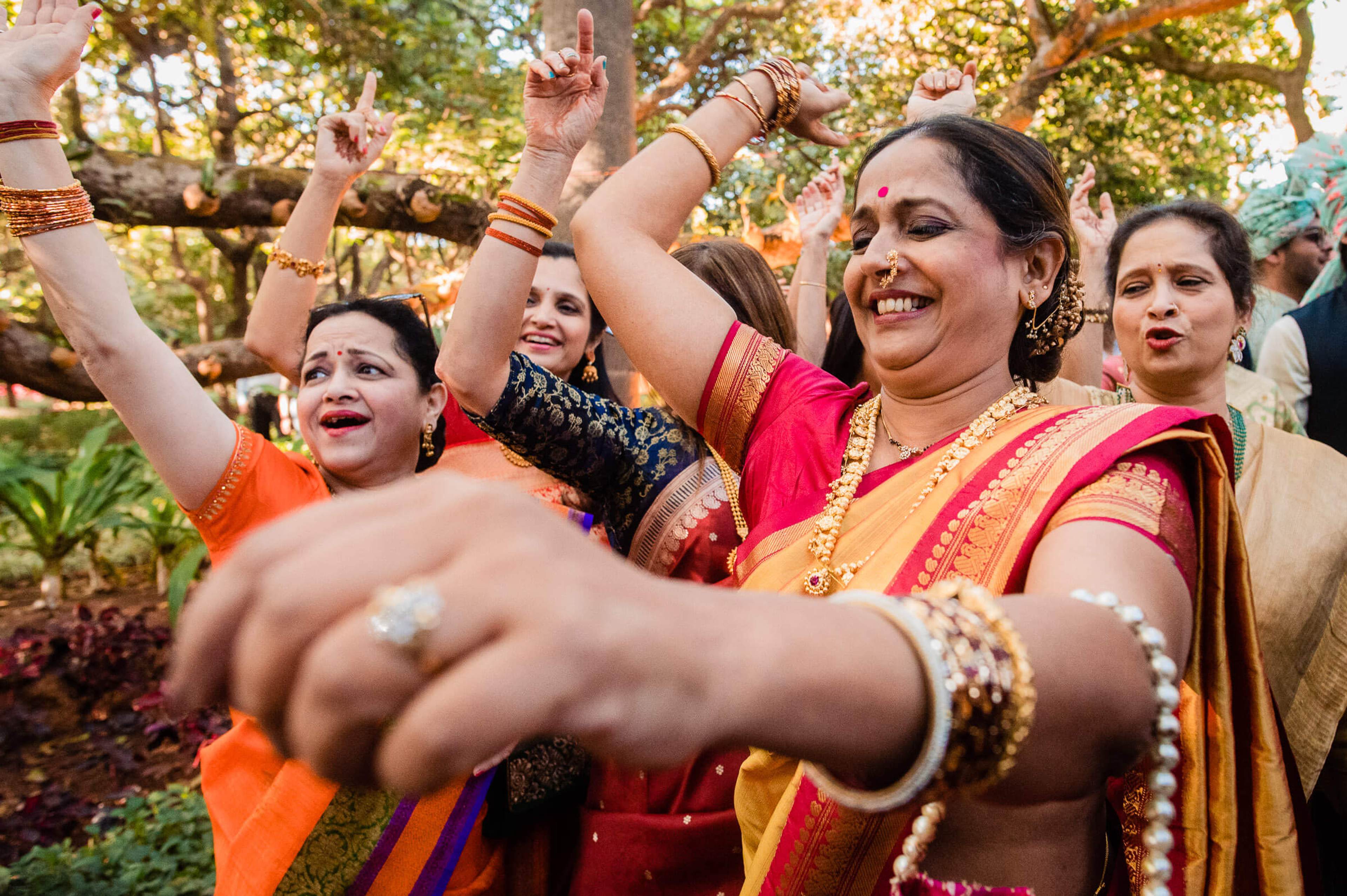 Women in colorful traditional Indian attire celebrating with raised arms in lush green garden at Mahabaleshwar