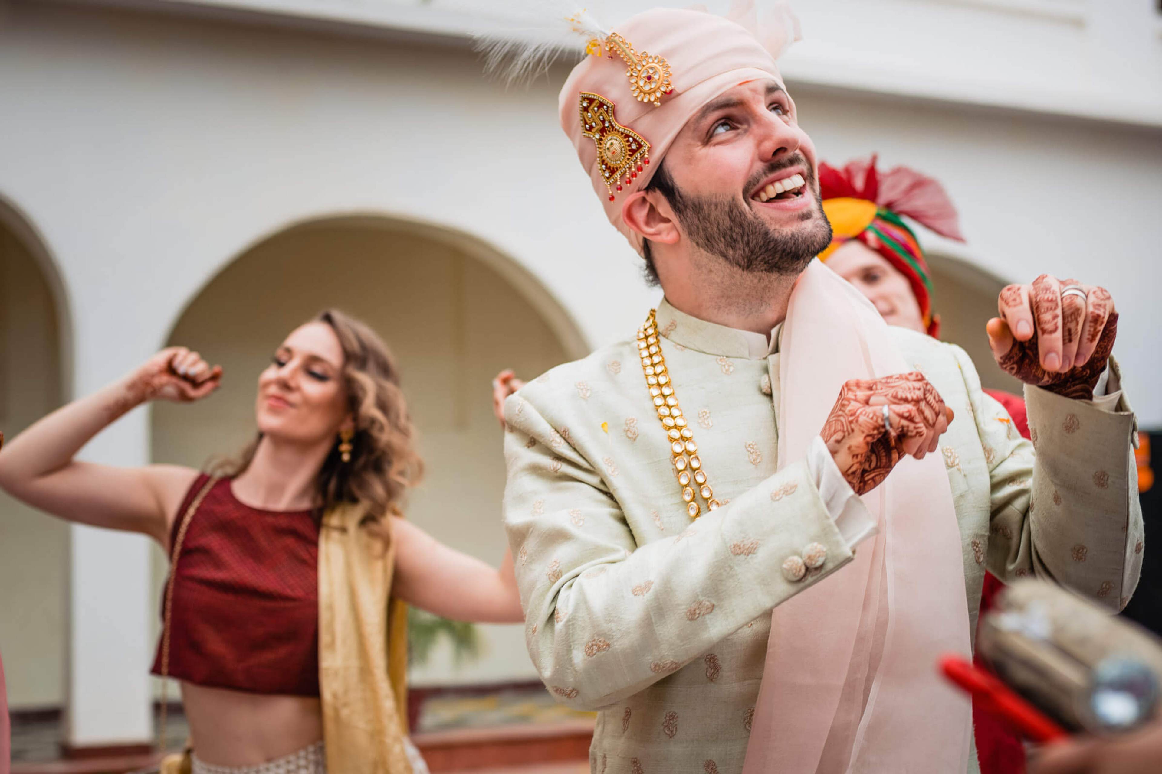 Groom Eric in ornate cream sherwani dancing with Maitrayee in burgundy at Rajasthan celebration