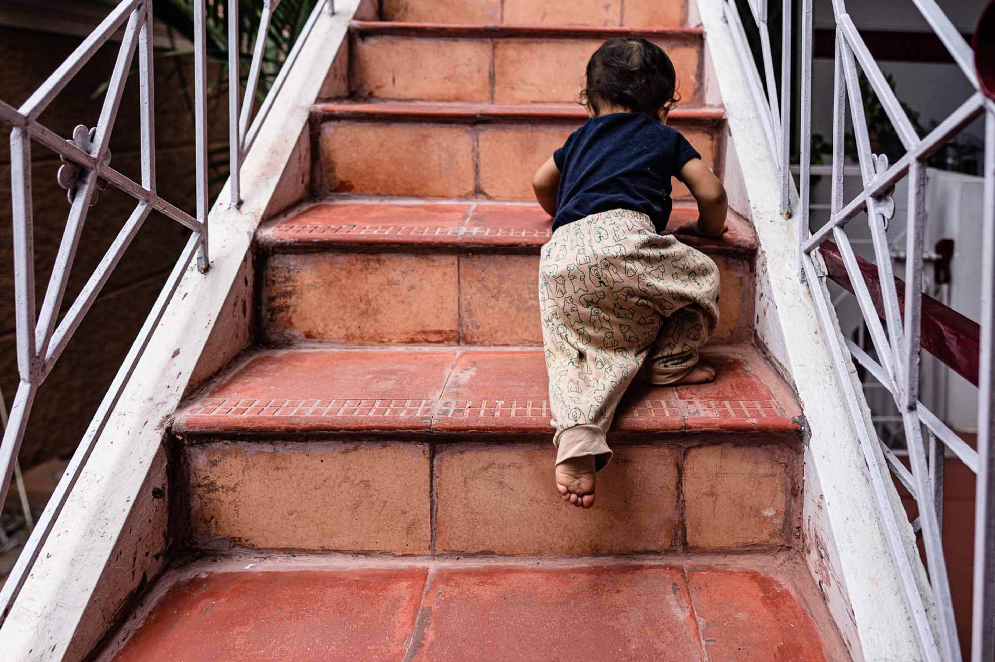 Child climbing red brick stairs between white metal railings, viewed from above