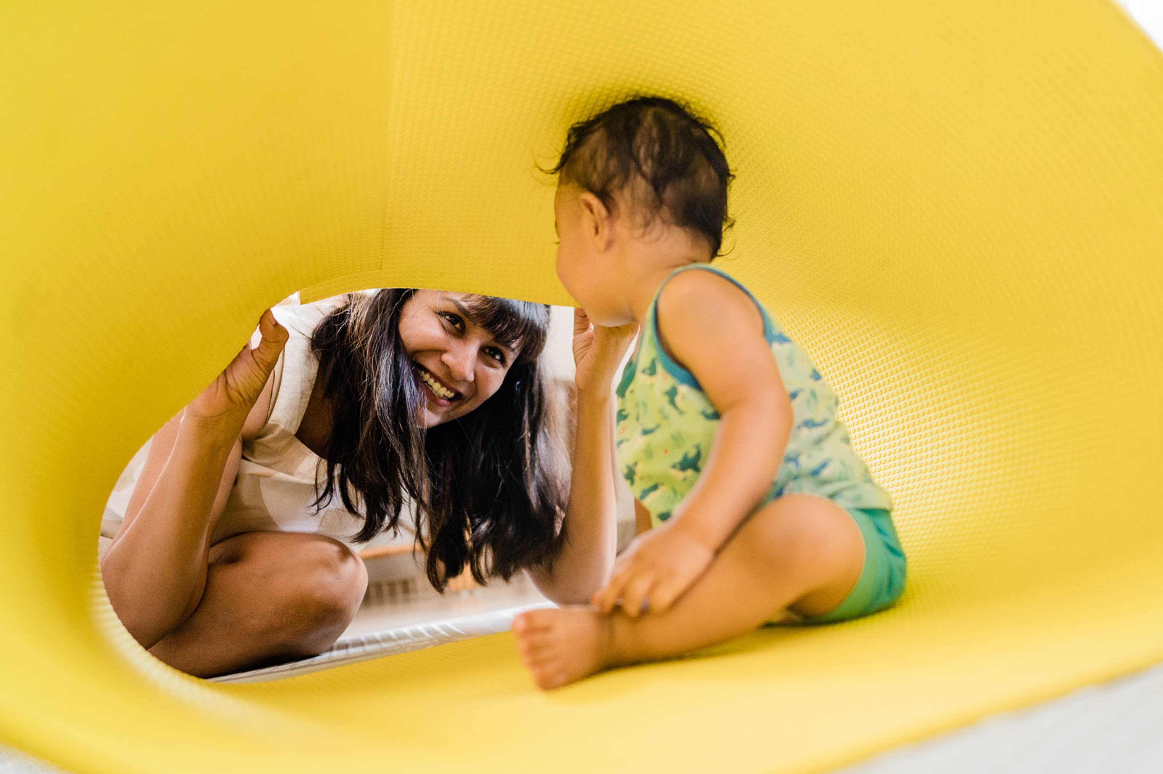 Woman and child playing together inside a bright yellow tunnel structure, smiling and interacting