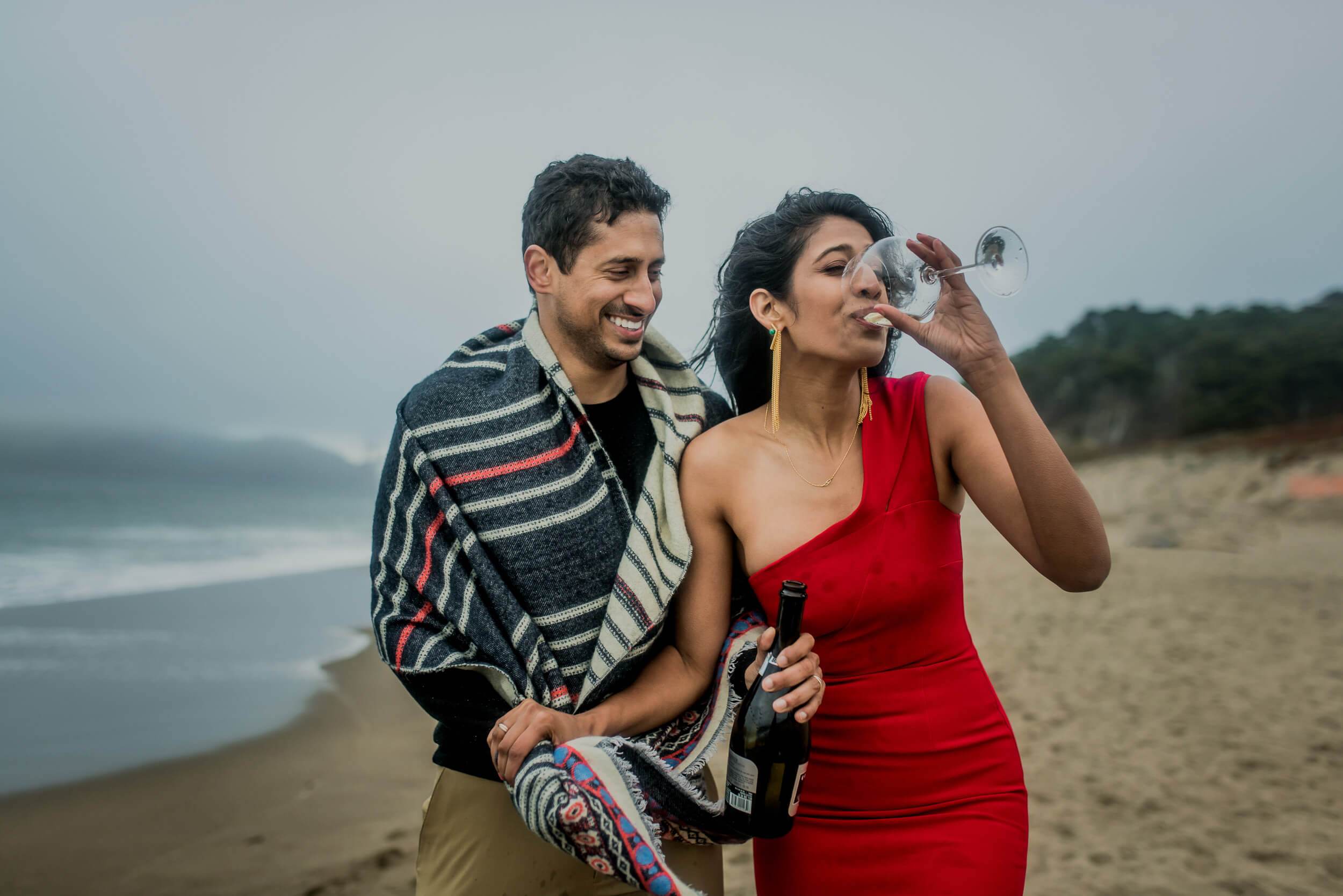 Anu and Raghu walk along a California beach in casual attire, laughing together at sunset