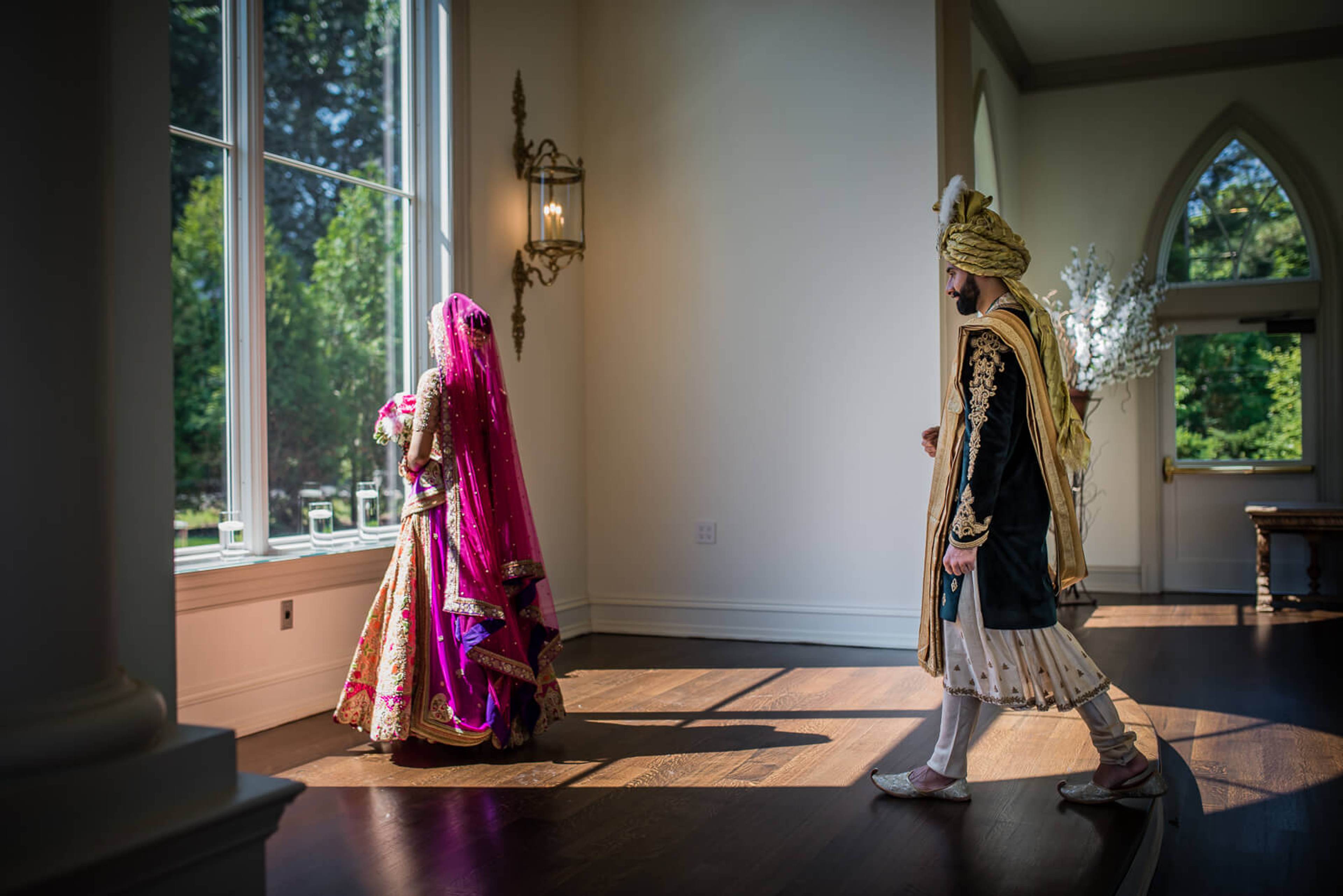 Barkha in magenta lehenga and Ankit in gold sherwani face each other in sunlit room, New York