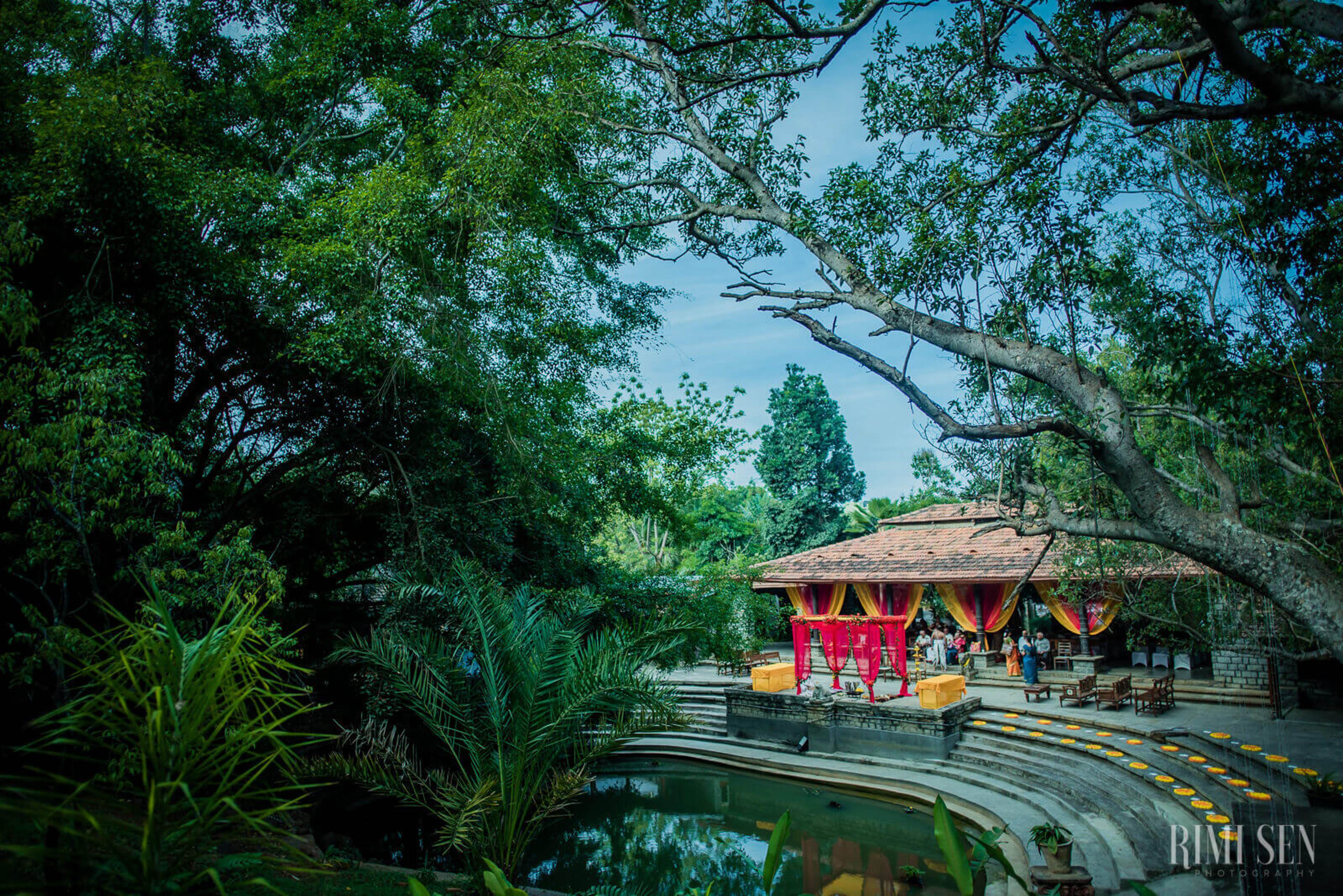 Red pavilion temple beside still water under lush green canopy trees, Bangalore