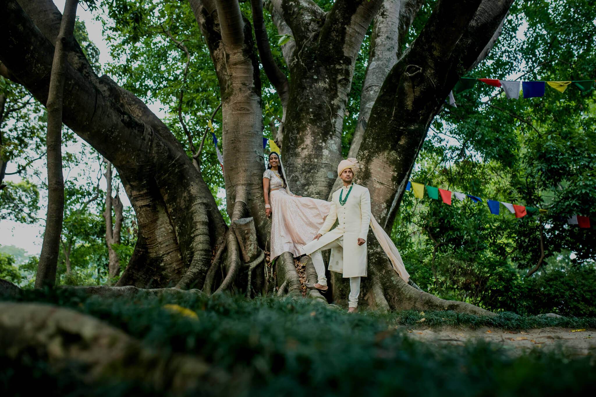 Anu and Raghu stand beneath a massive tree in Nepal, her veil flowing in the breeze