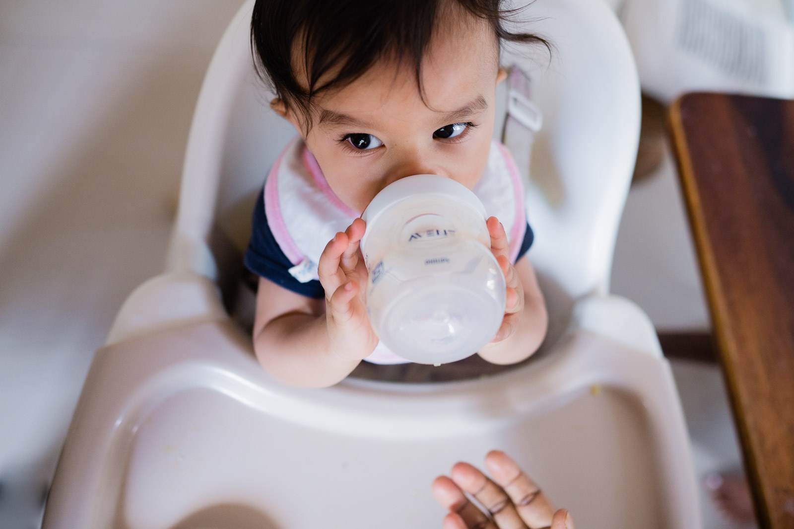 Toddler in high chair holding sippy cup, looking down at camera