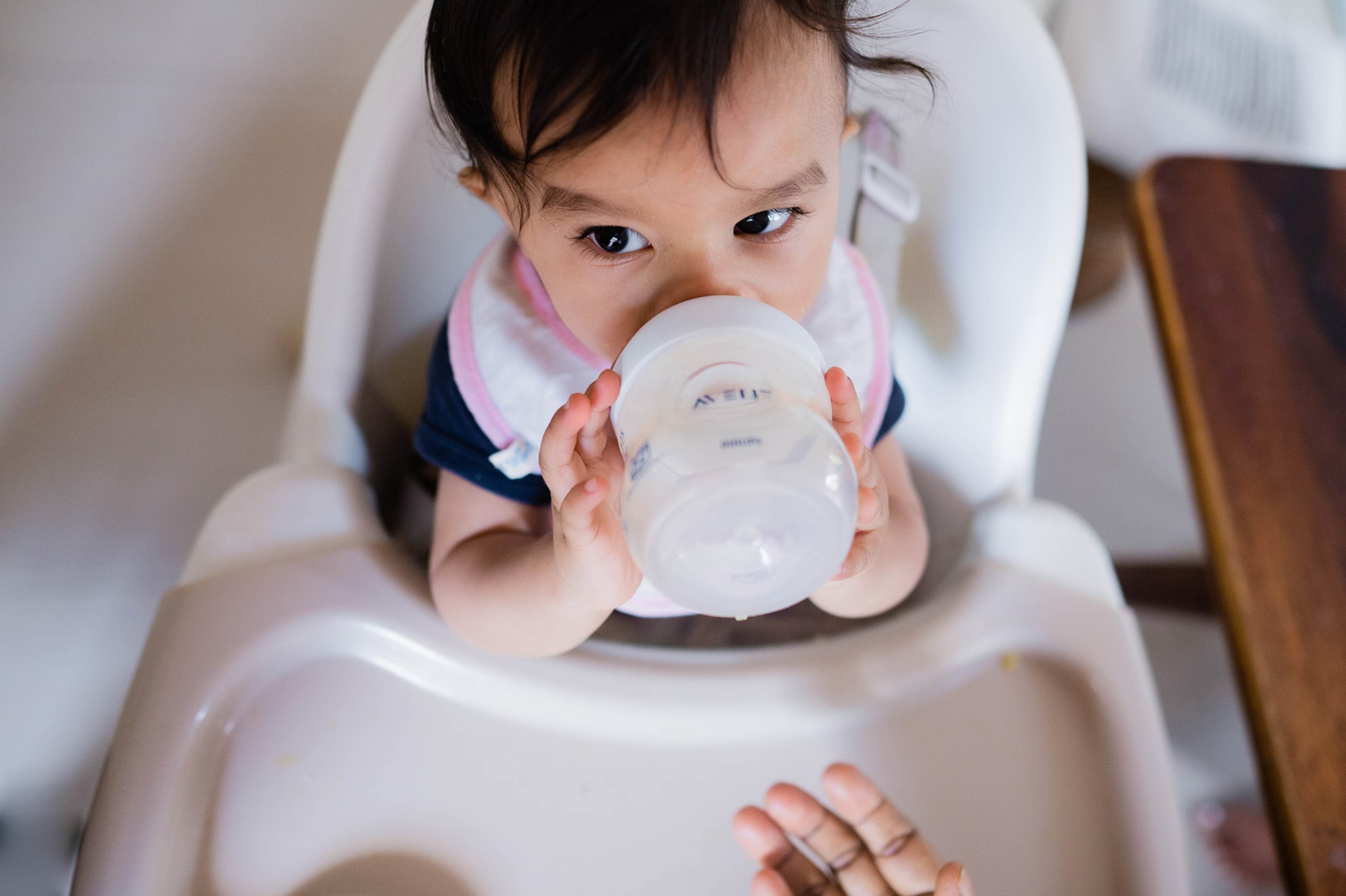 Toddler in high chair holding sippy cup, looking down at camera