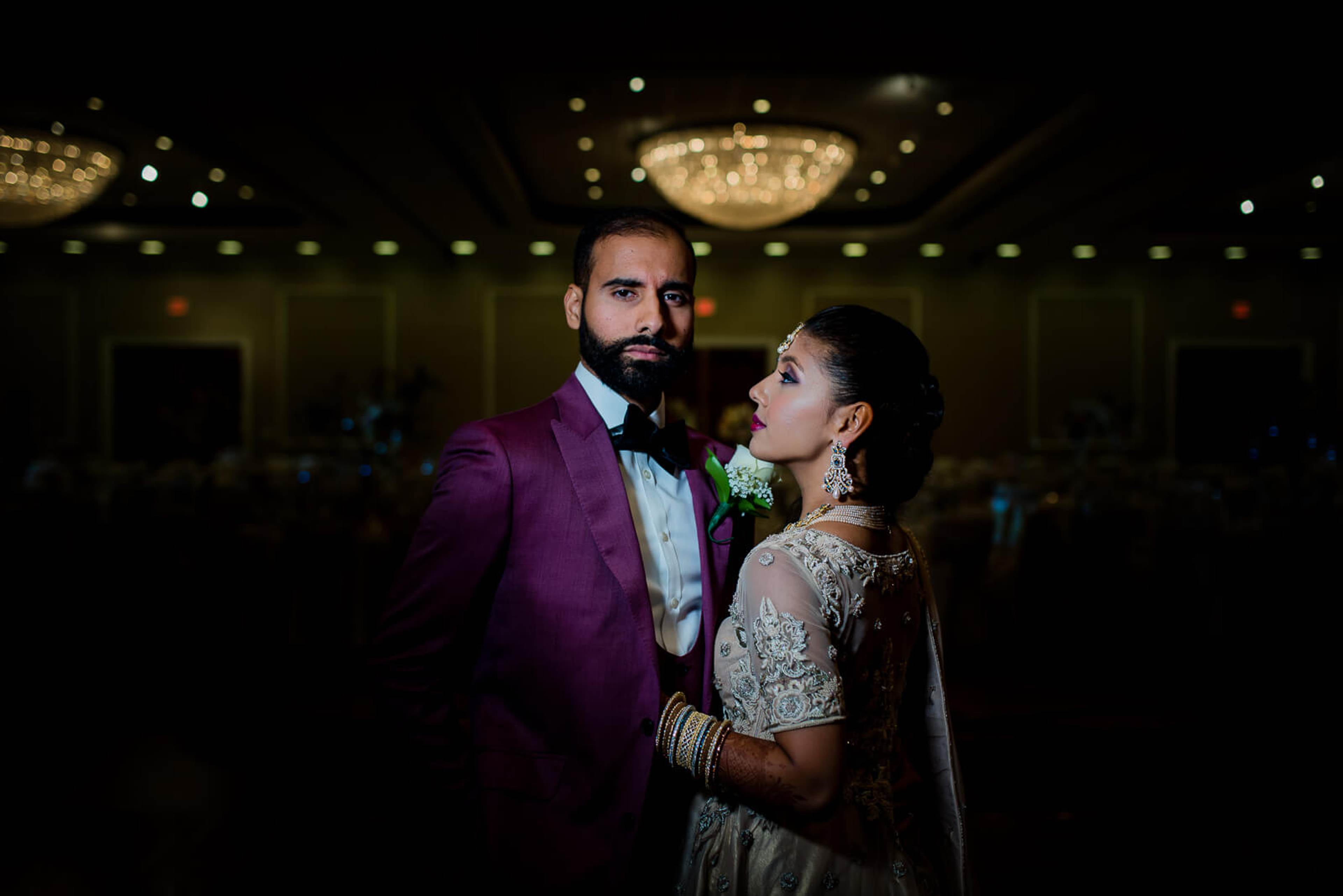 Barkha and Ankit stand under ornate chandeliers in elegant wedding attire at a New York ballroom