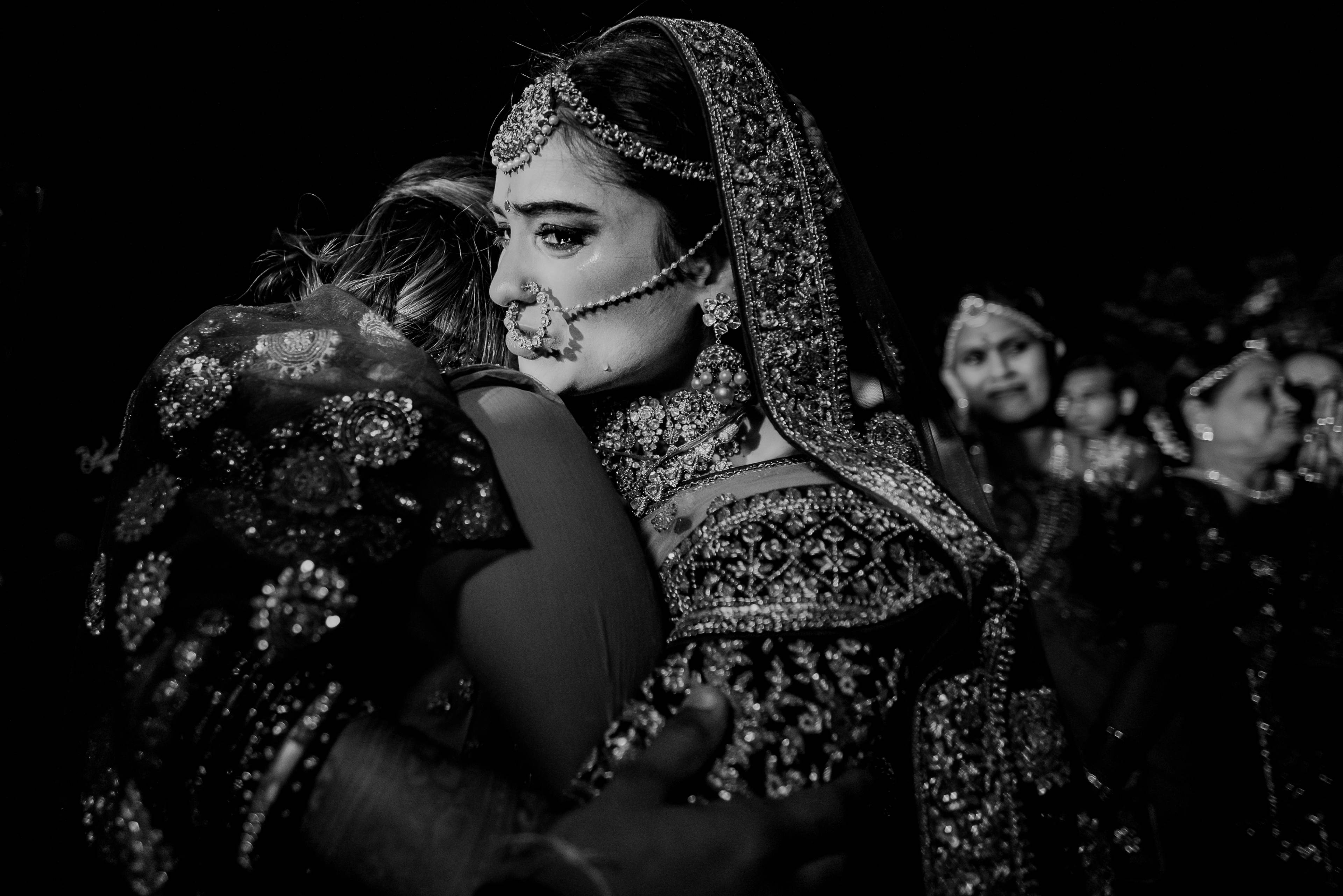 Bride in ornate embroidered veil and jewelry embraces child in black and white portrait