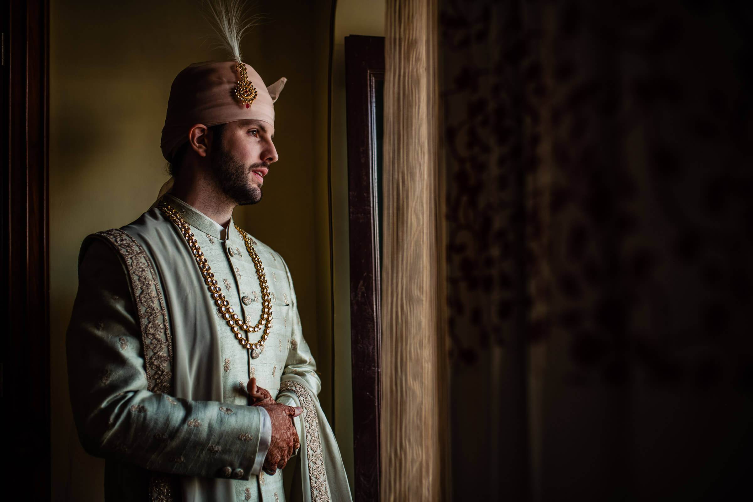 Eric in traditional Rajasthani attire with feathered headpiece, standing in warm doorway light