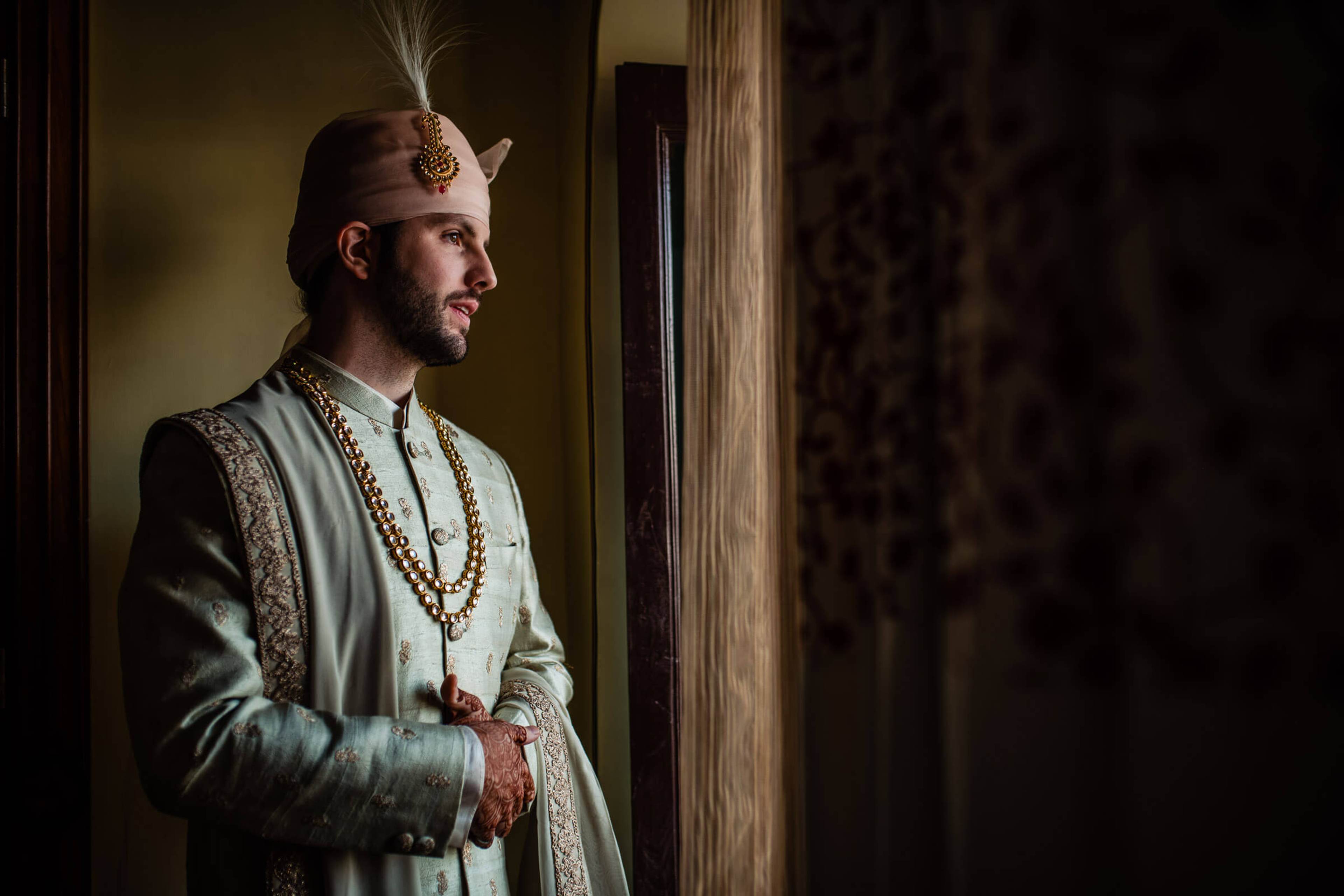 Eric in traditional Rajasthani attire with feathered headpiece, standing in warm doorway light