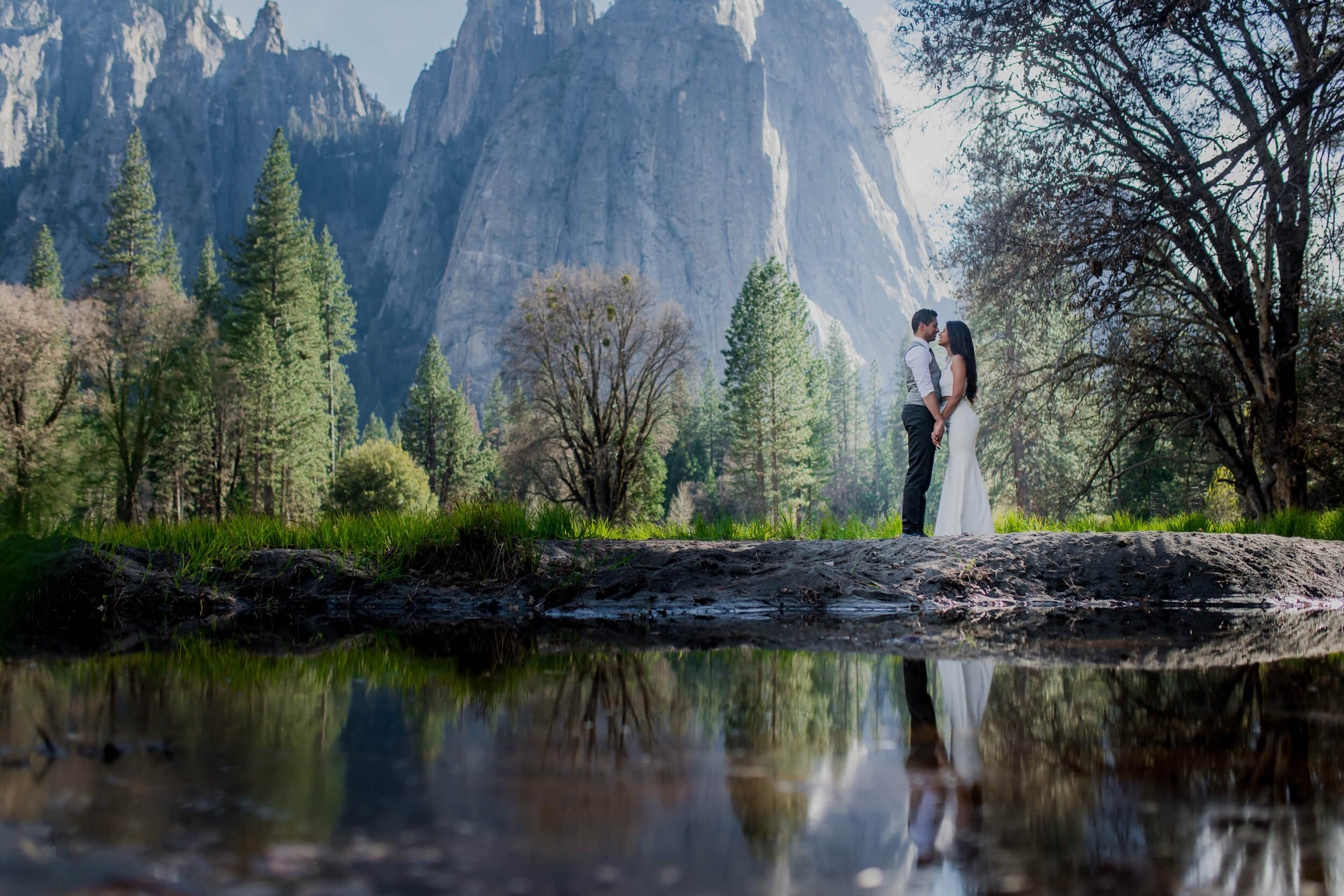 Couple embracing by river with towering granite cliffs and forest in California landscape