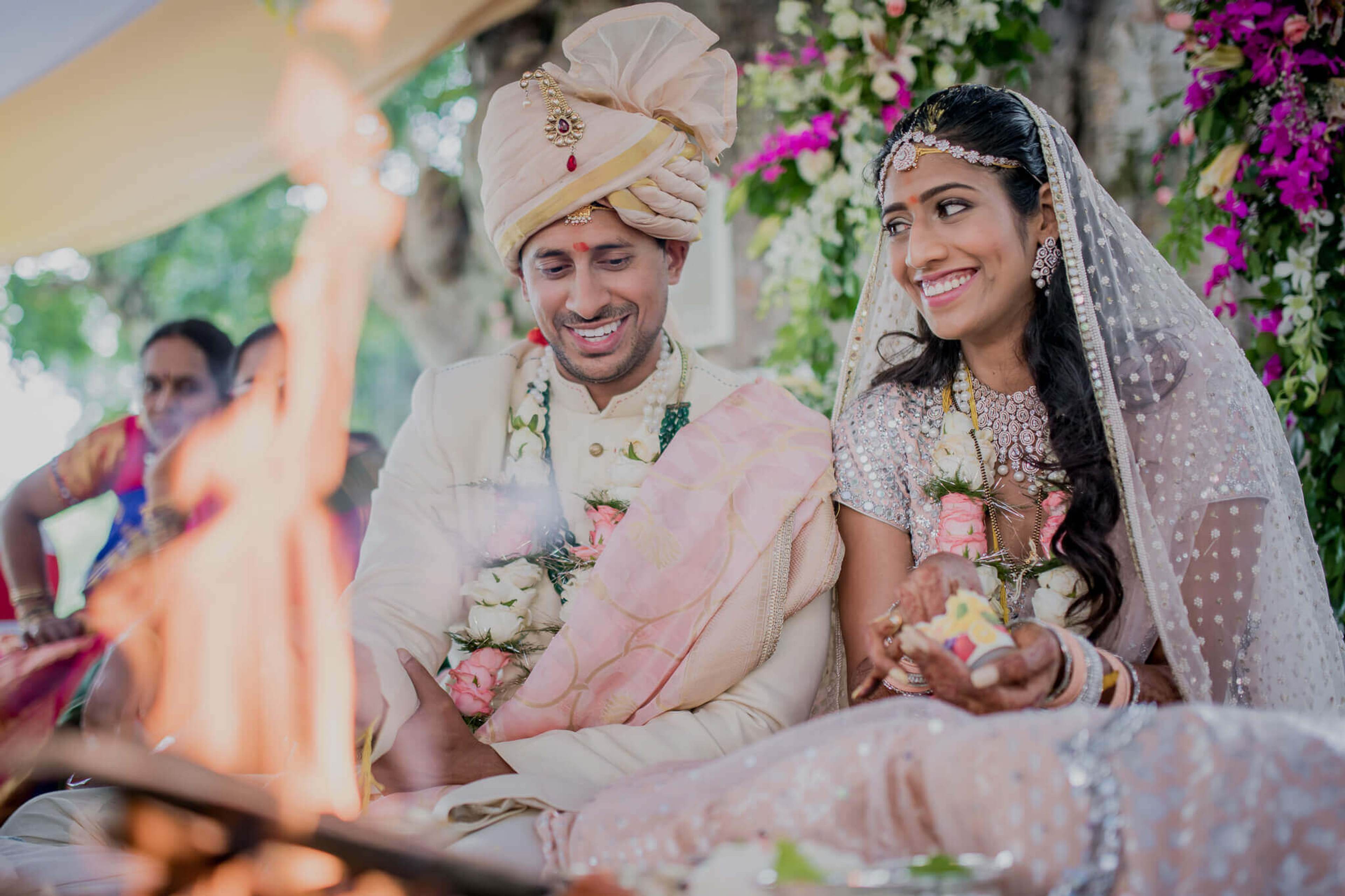 Anu and Raghu smile during their wedding ceremony in Nepal, surrounded by pink flowers and garlands