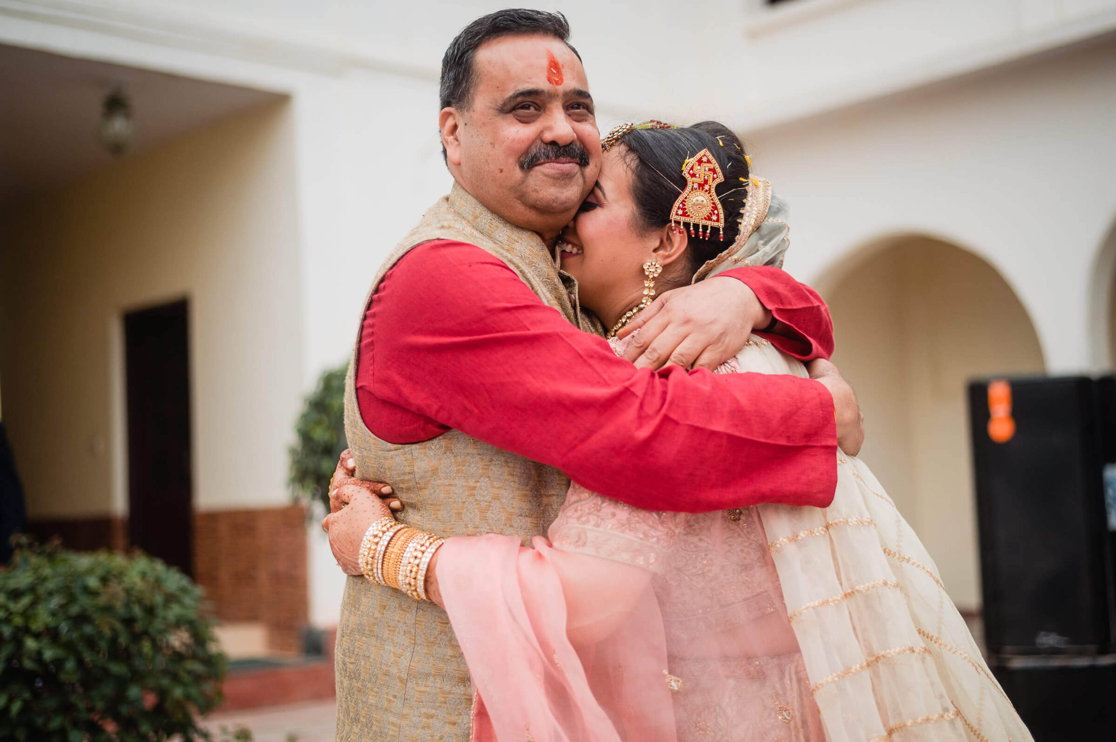 Maitrayee and Eric embrace in traditional Indian wedding attire at a Rajasthan venue with white arched walls