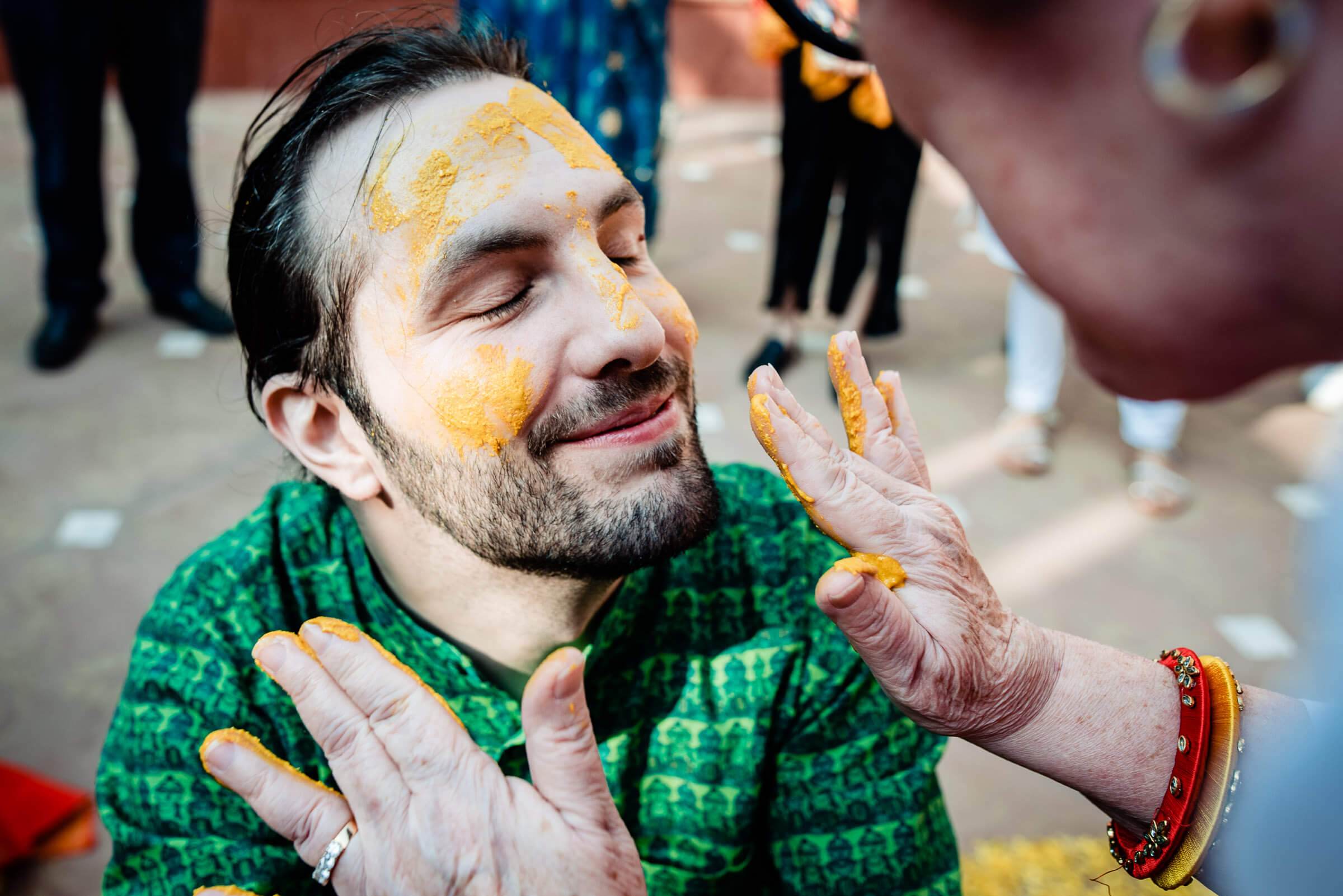 Man wearing green traditional attire with turmeric paste on face and hands during Rajasthan wedding celebration