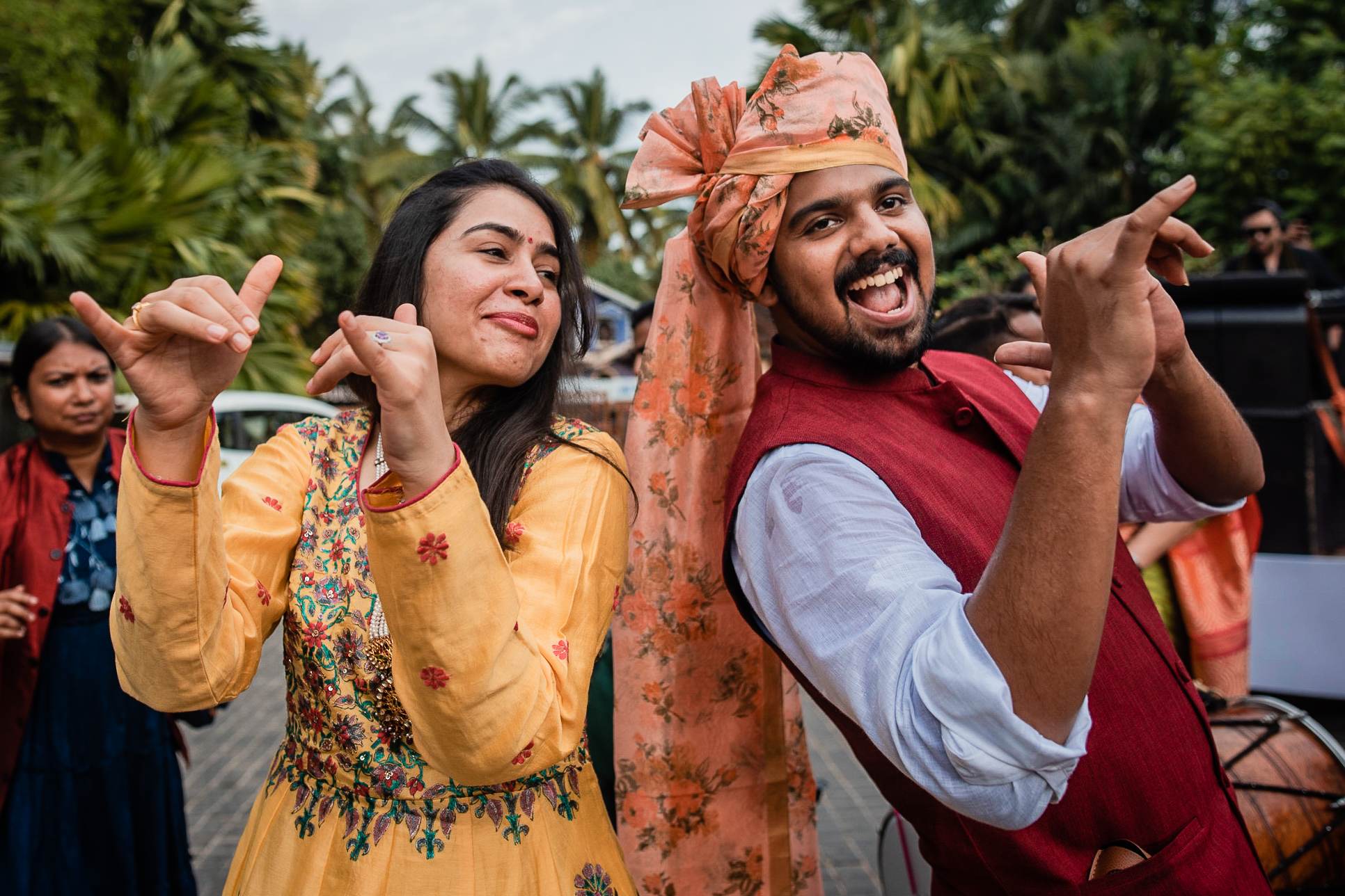 Avani and Srikant dancing joyfully in traditional attire amid tropical palms at their Goa celebration