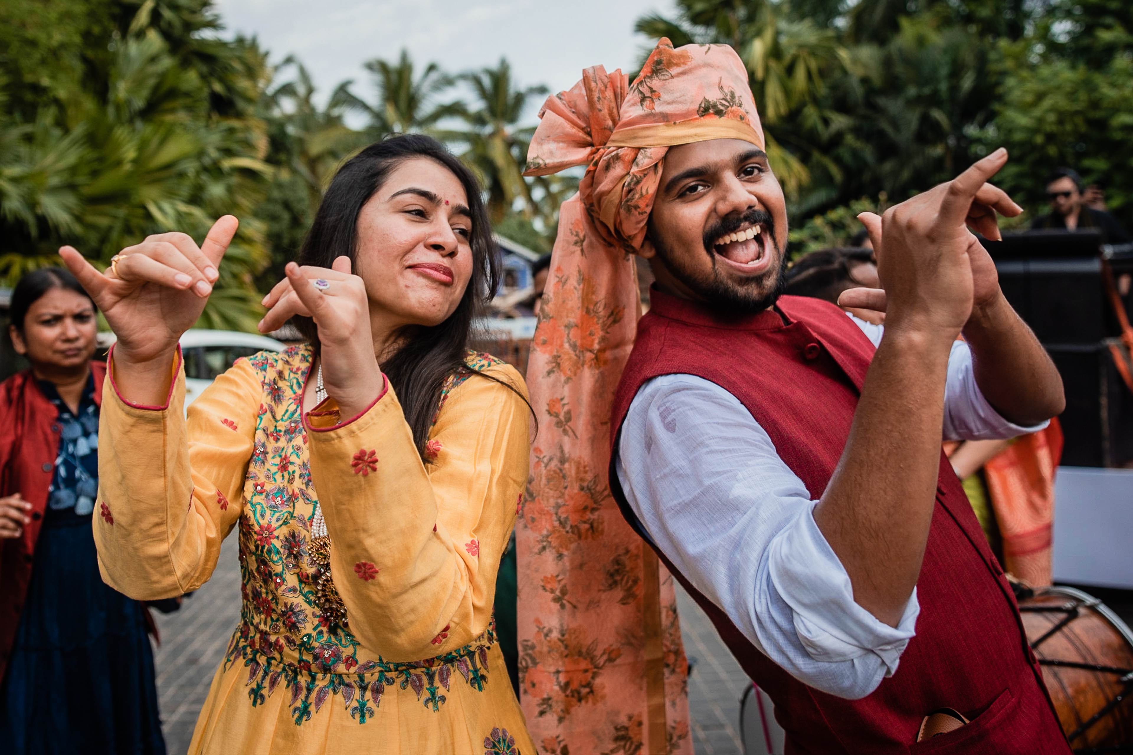 Avani and Srikant dancing joyfully in traditional attire amid tropical palms at their Goa celebration
