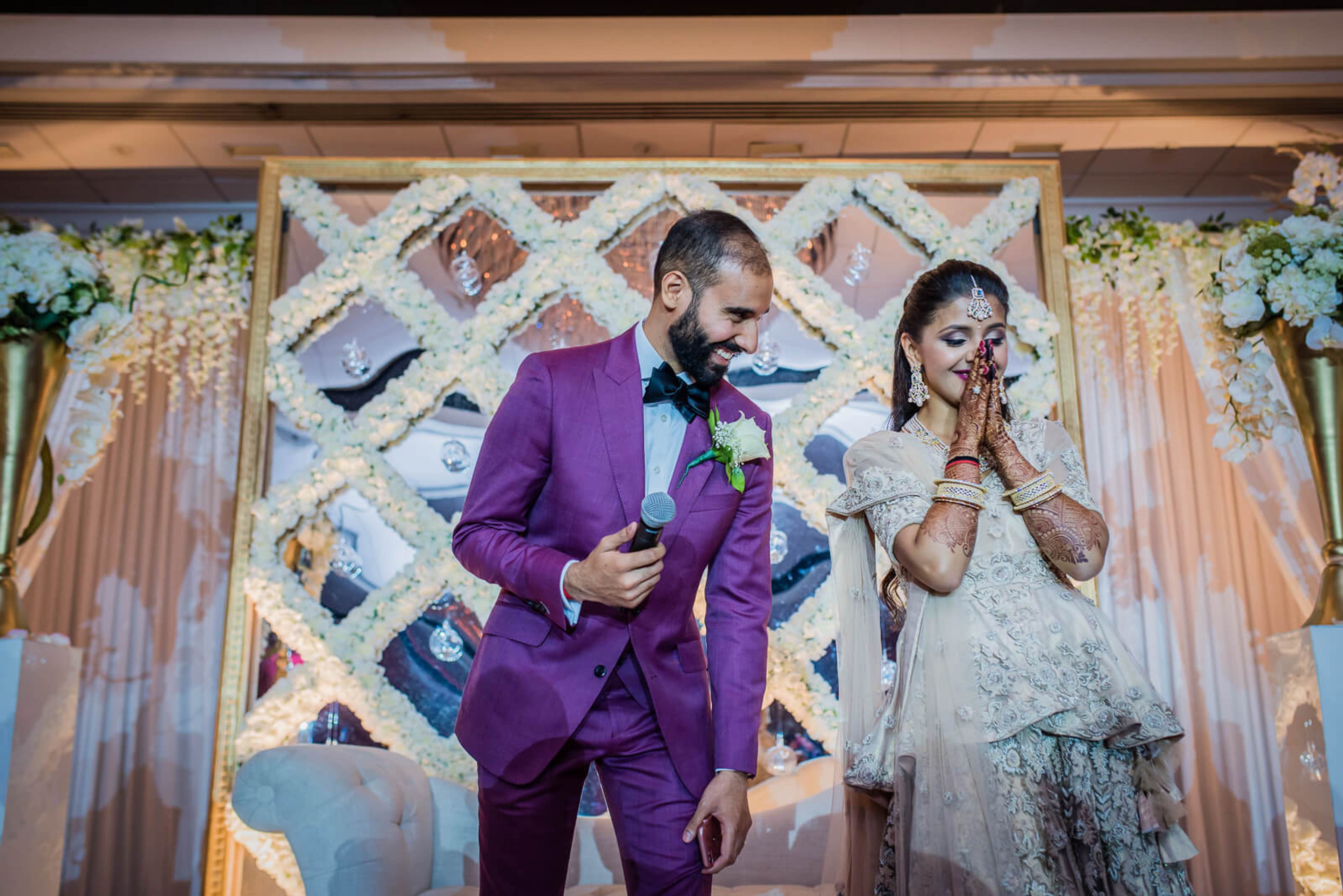 Barkha and Ankit stand before an ornate backdrop at their New York wedding ceremony, she in white lace, he in purple suit