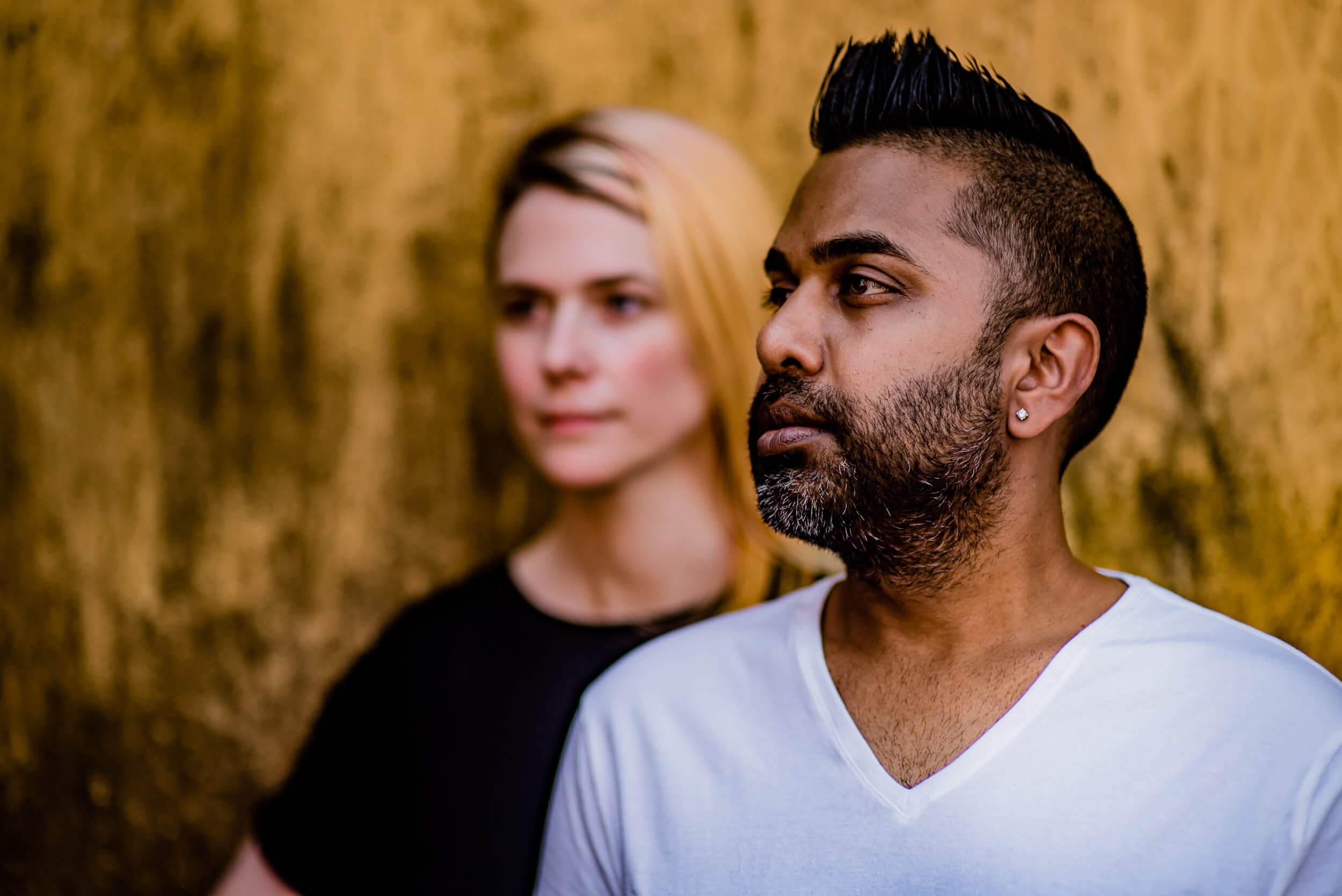 Sarah and Ravin stand against a golden textured wall in Goa, warm light highlighting their thoughtful expressions