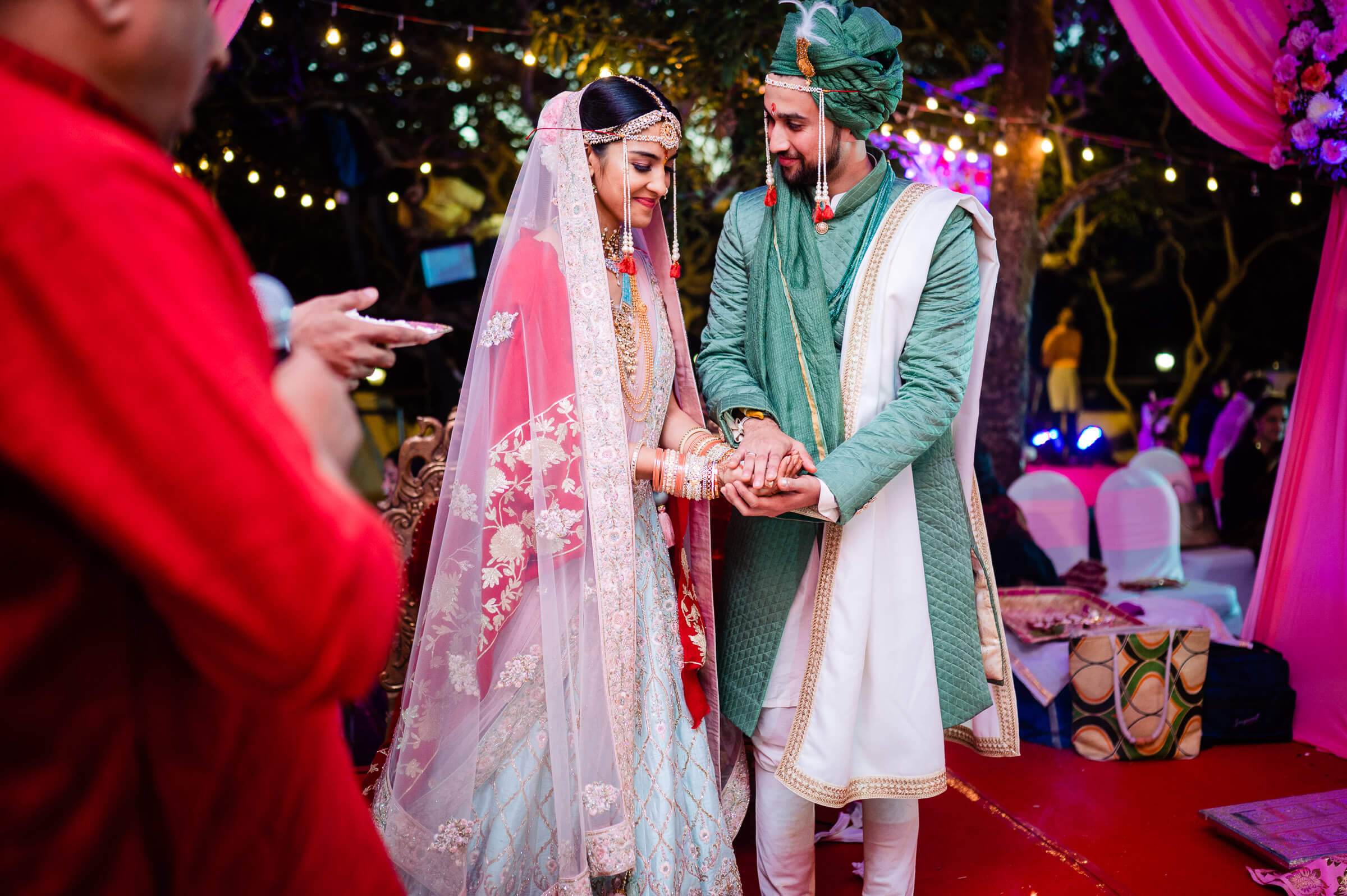 Shreya and Yash exchange hands in traditional wedding attire at vibrant Mahabaleshwar celebration with colorful lights