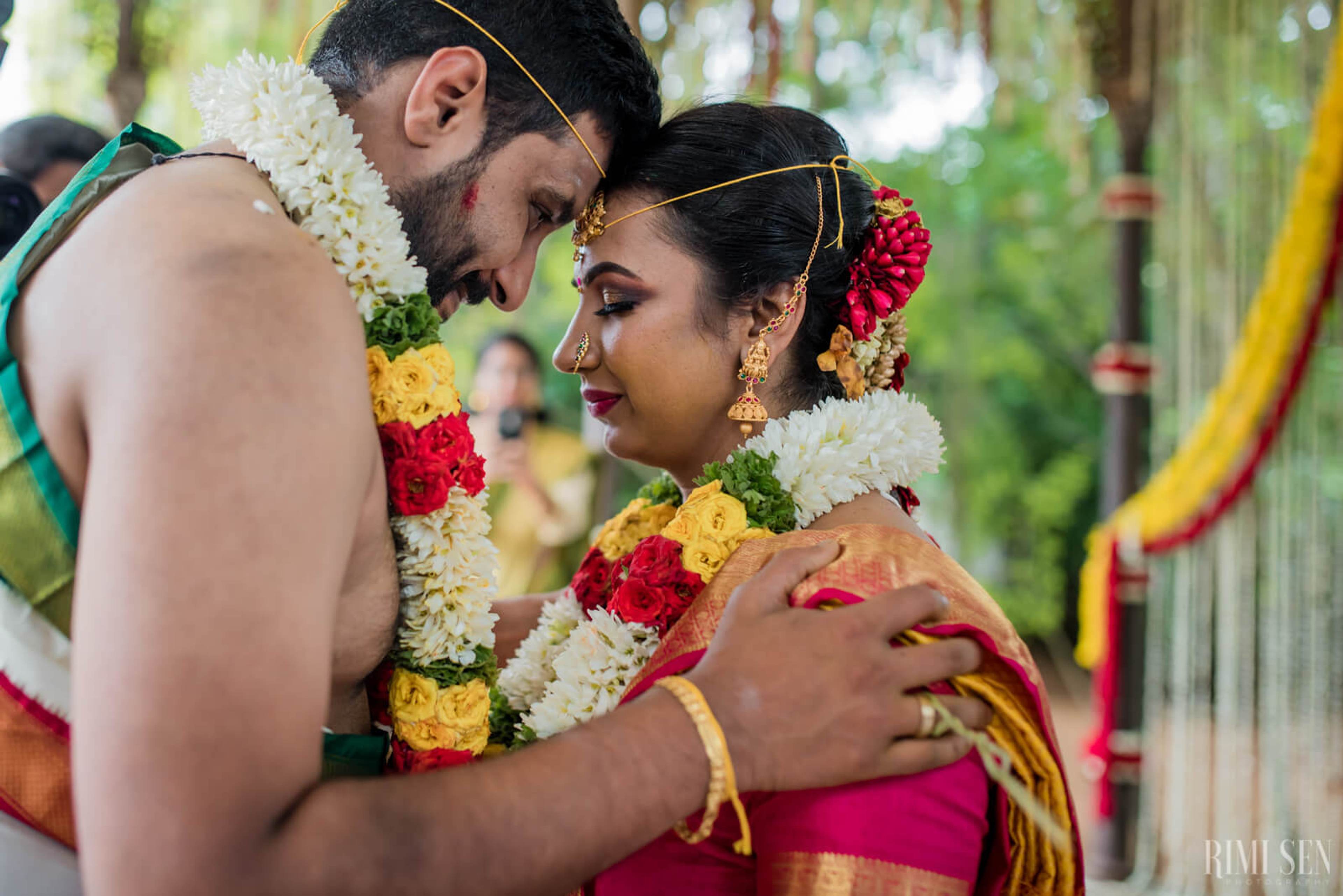 Nivetha and Sridhar embrace wearing colorful flower garlands at their Bangalore wedding ceremony