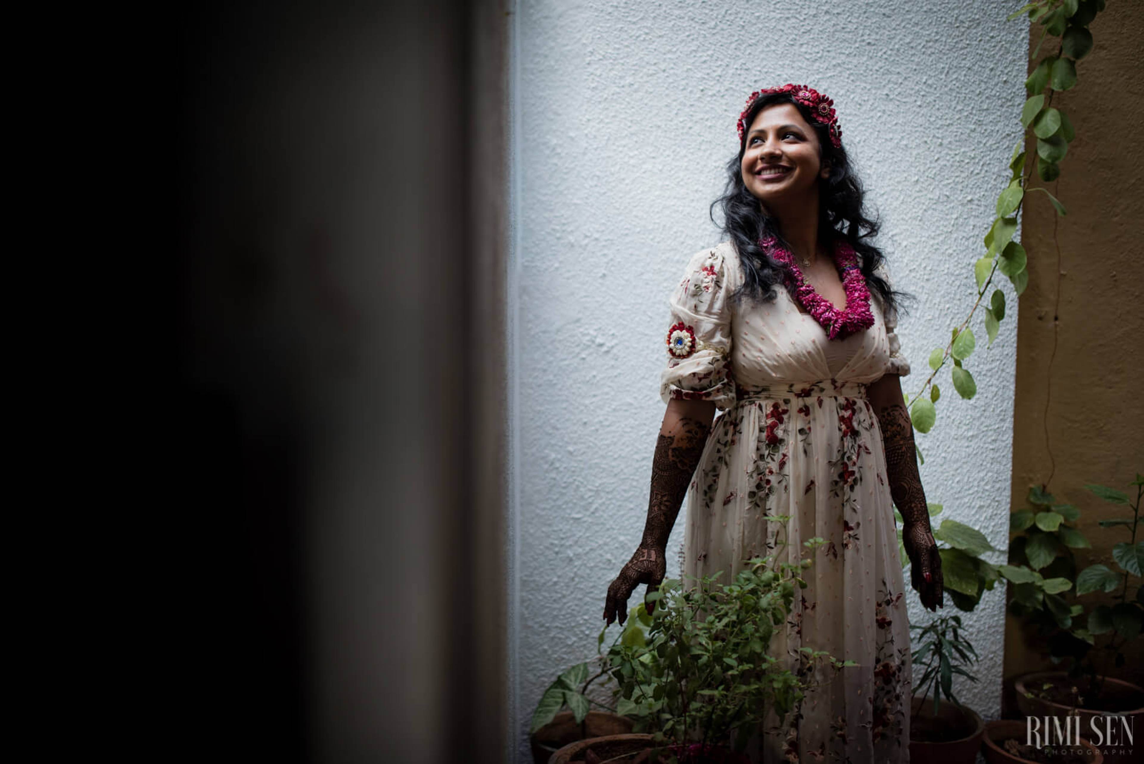 Nivetha stands in traditional attire with floral garland, smiling against white wall with climbing ivy