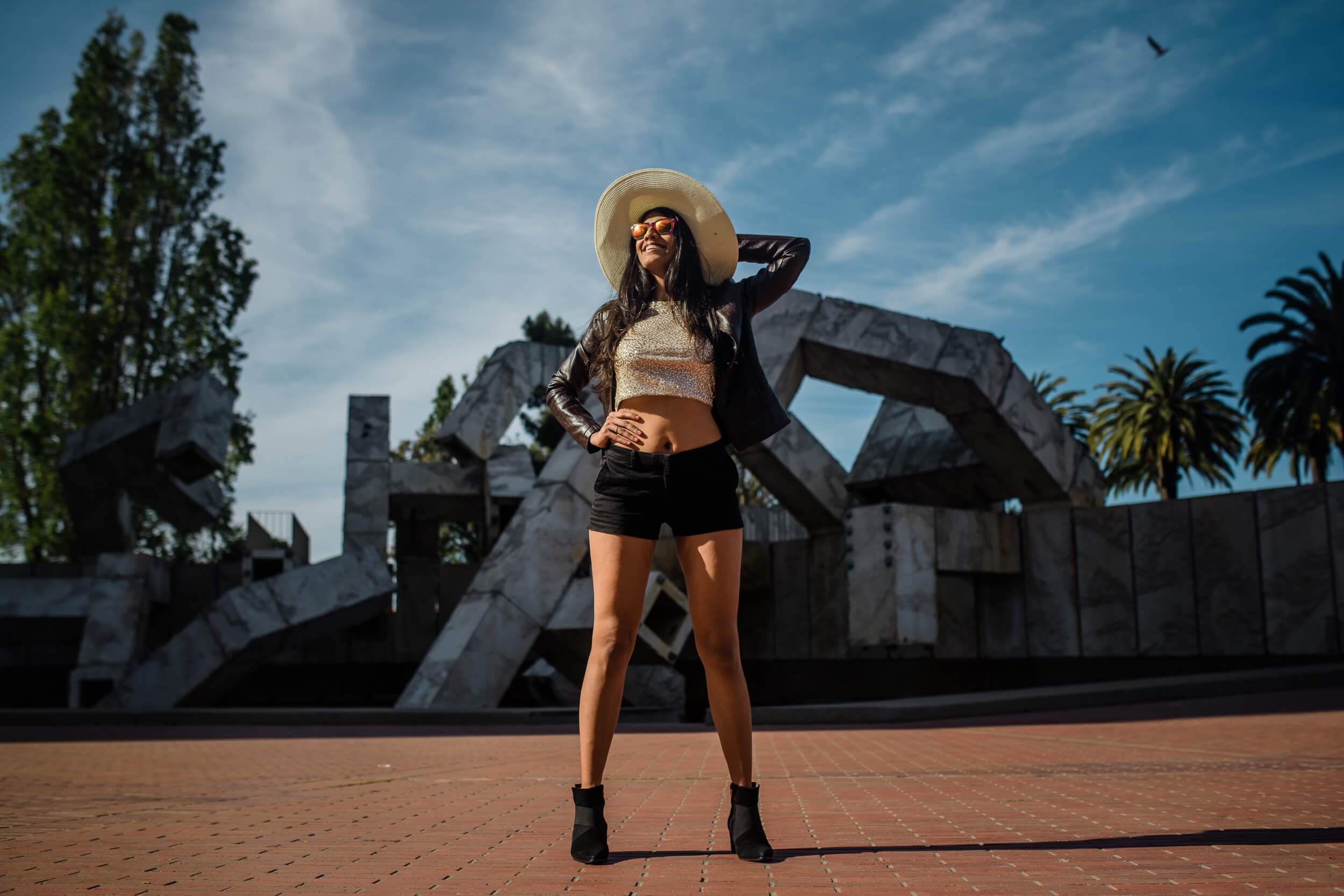 Woman in straw hat and black crop top poses at California sculpture park under blue sky