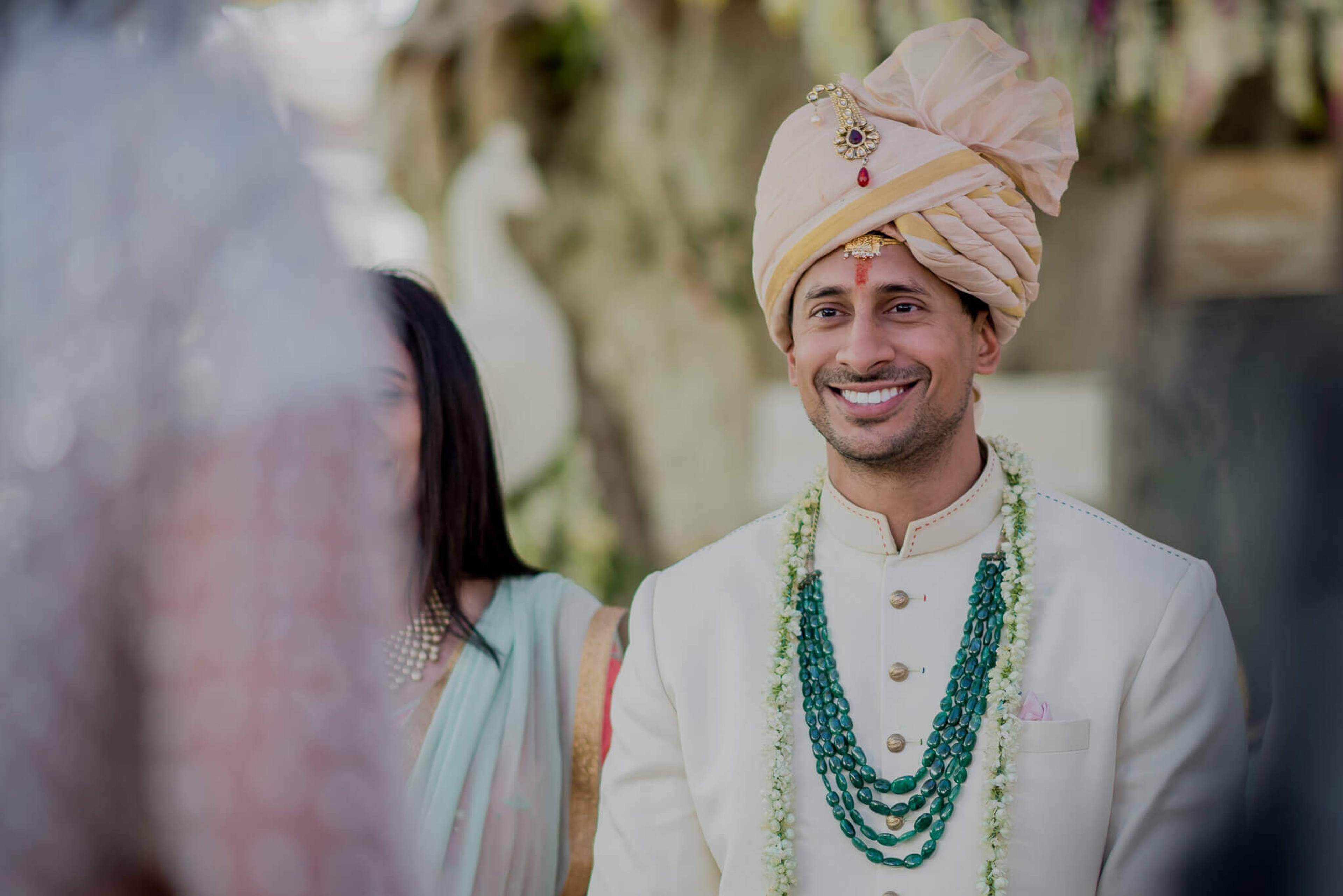 Groom Raghu smiling in cream sherwani and turban with floral garland, Nepal wedding