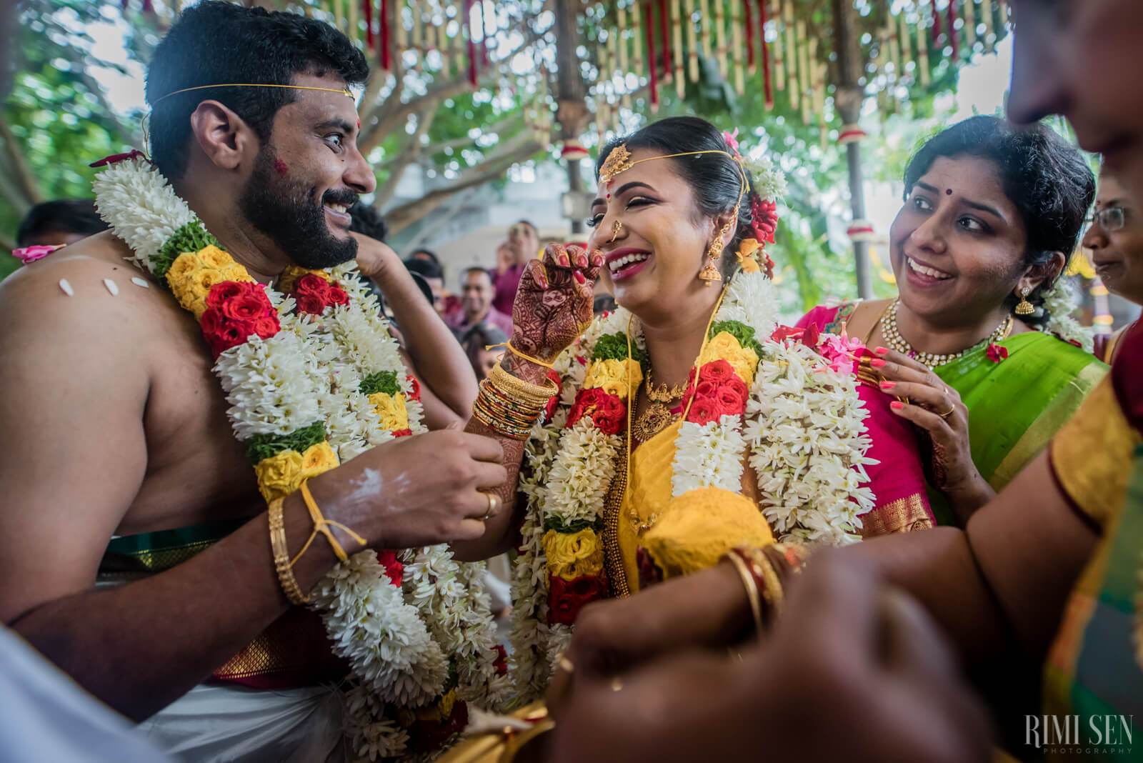 Nivetha and Sridhar laugh together wearing vibrant flower garlands at their Bangalore wedding celebration