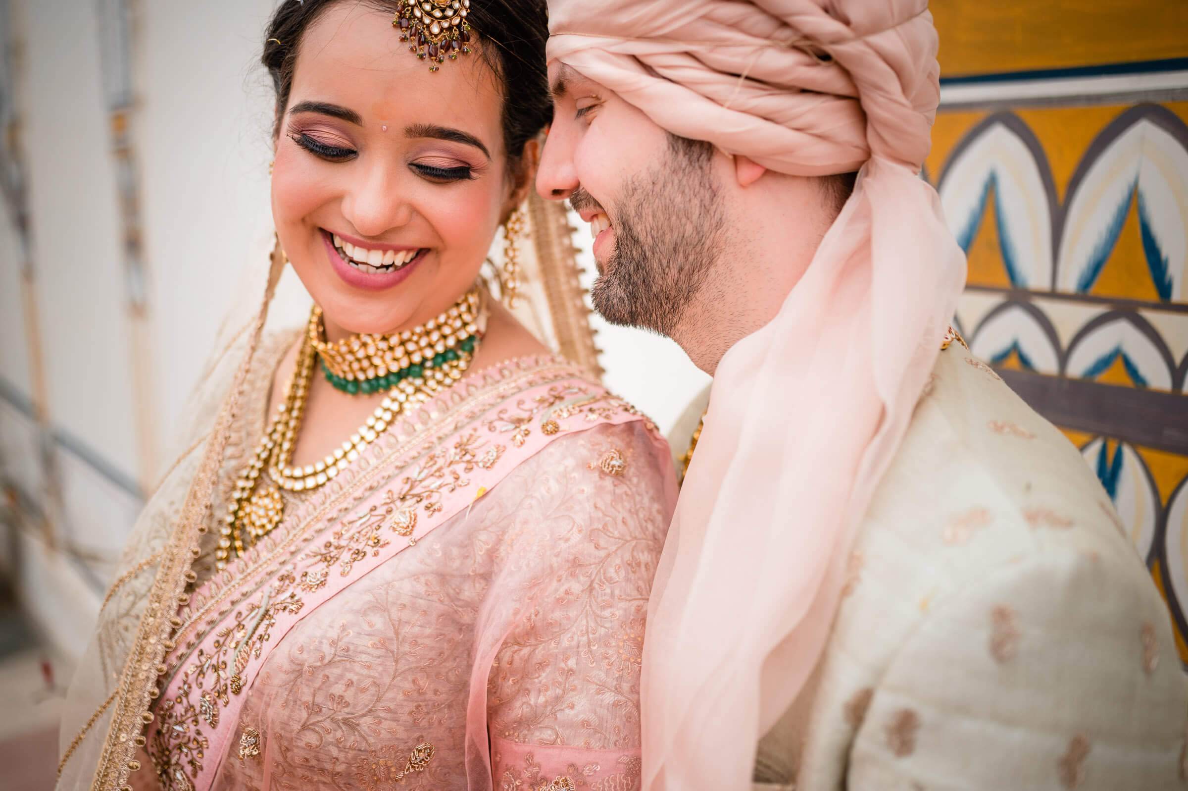 Maitrayee and Eric embrace in traditional wedding attire against ornate Rajasthan architecture
