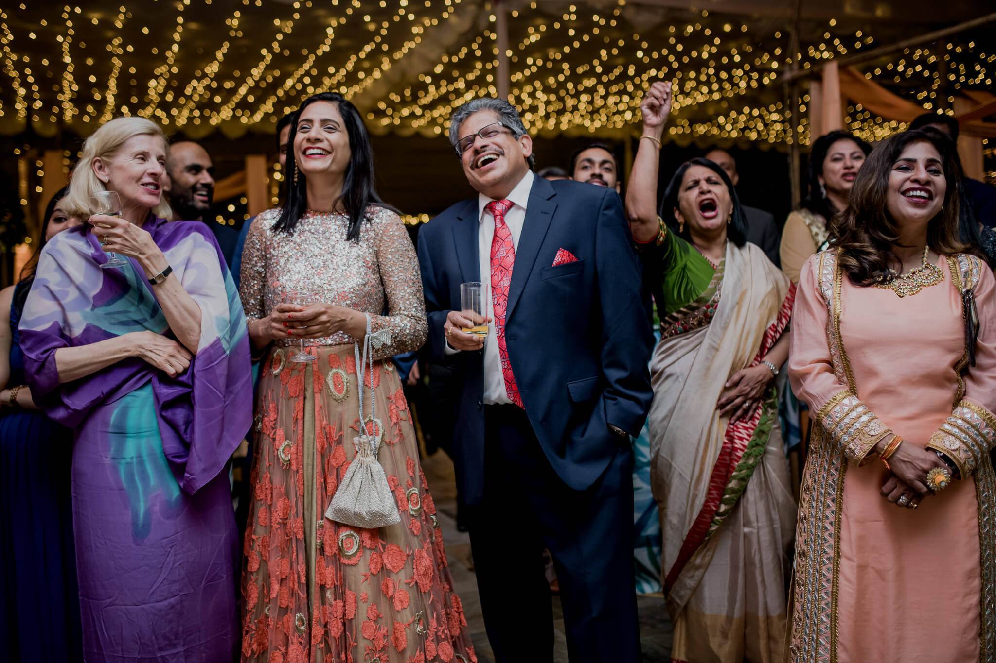 Anu and Raghu celebrate with smiling family and friends under golden string lights at their reception in Nepal