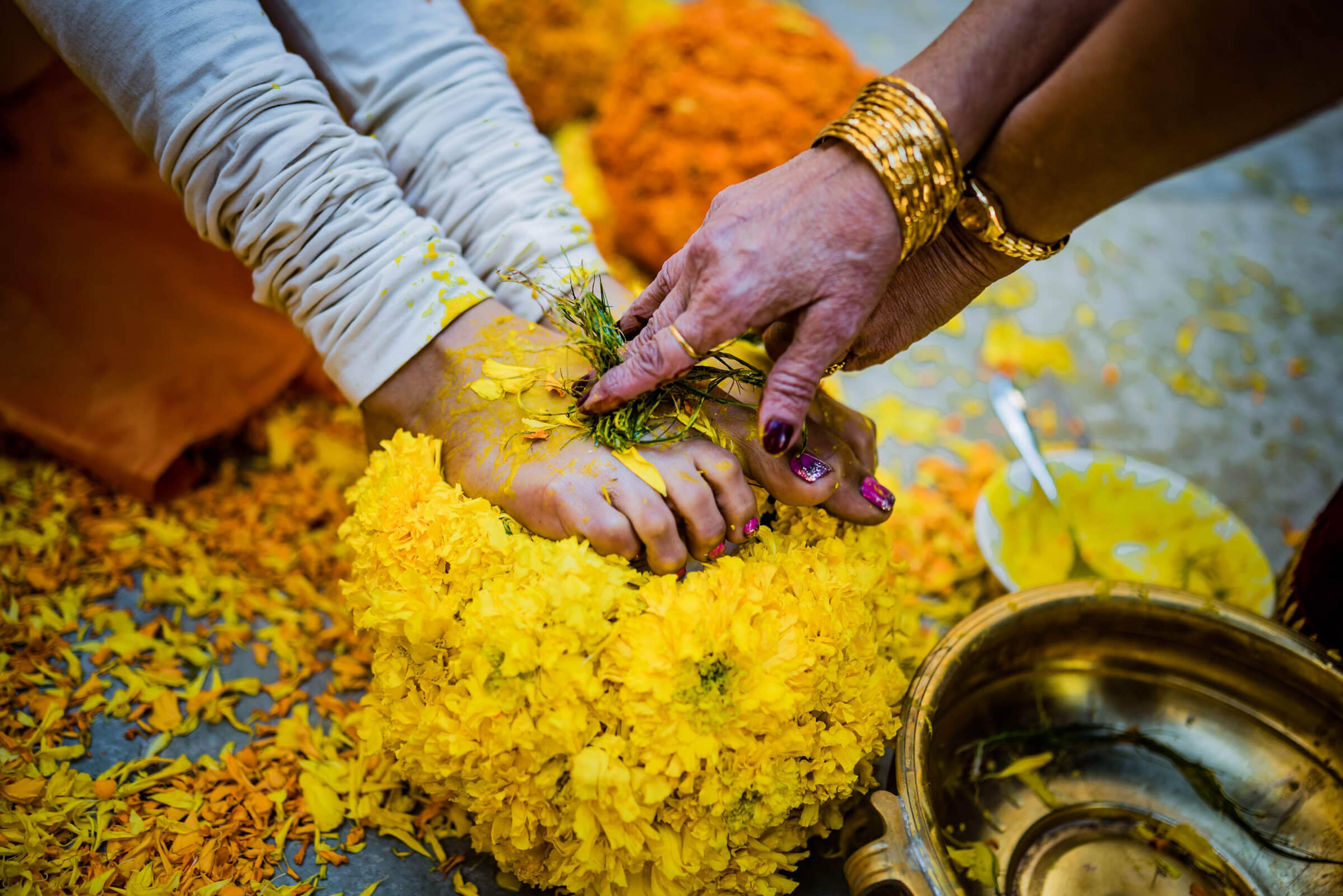Shreya and Yash's hands adorned with gold bangles and mehendi, nestled in bright yellow flowers at Mahabaleshwar