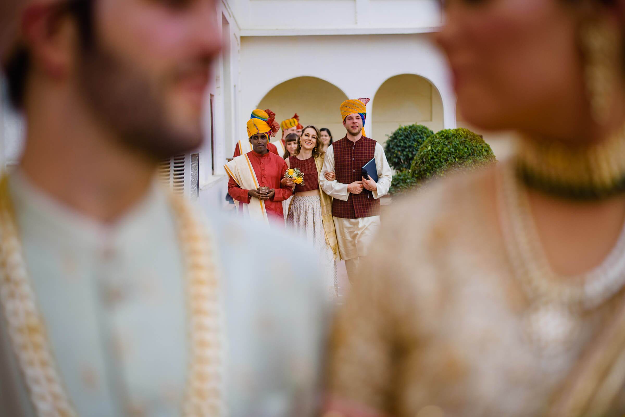 Maitrayee and Eric in traditional Rajasthani attire with guests at an archway during celebration