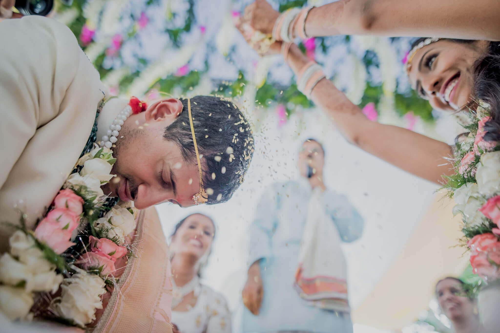 Anu & Raghu laugh while showering with flower petals, surrounded by colorful floral arrangements and loved ones in Nepal