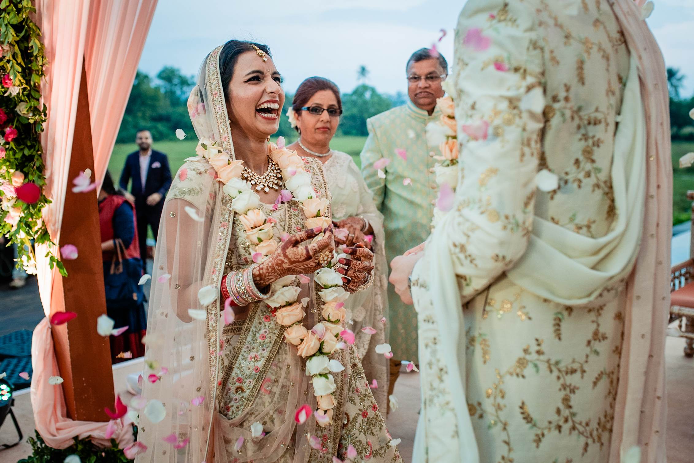 Avani smiles at the ceremony in Goa, wearing traditional embroidered attire and floral garland, with Srikant and family nearby