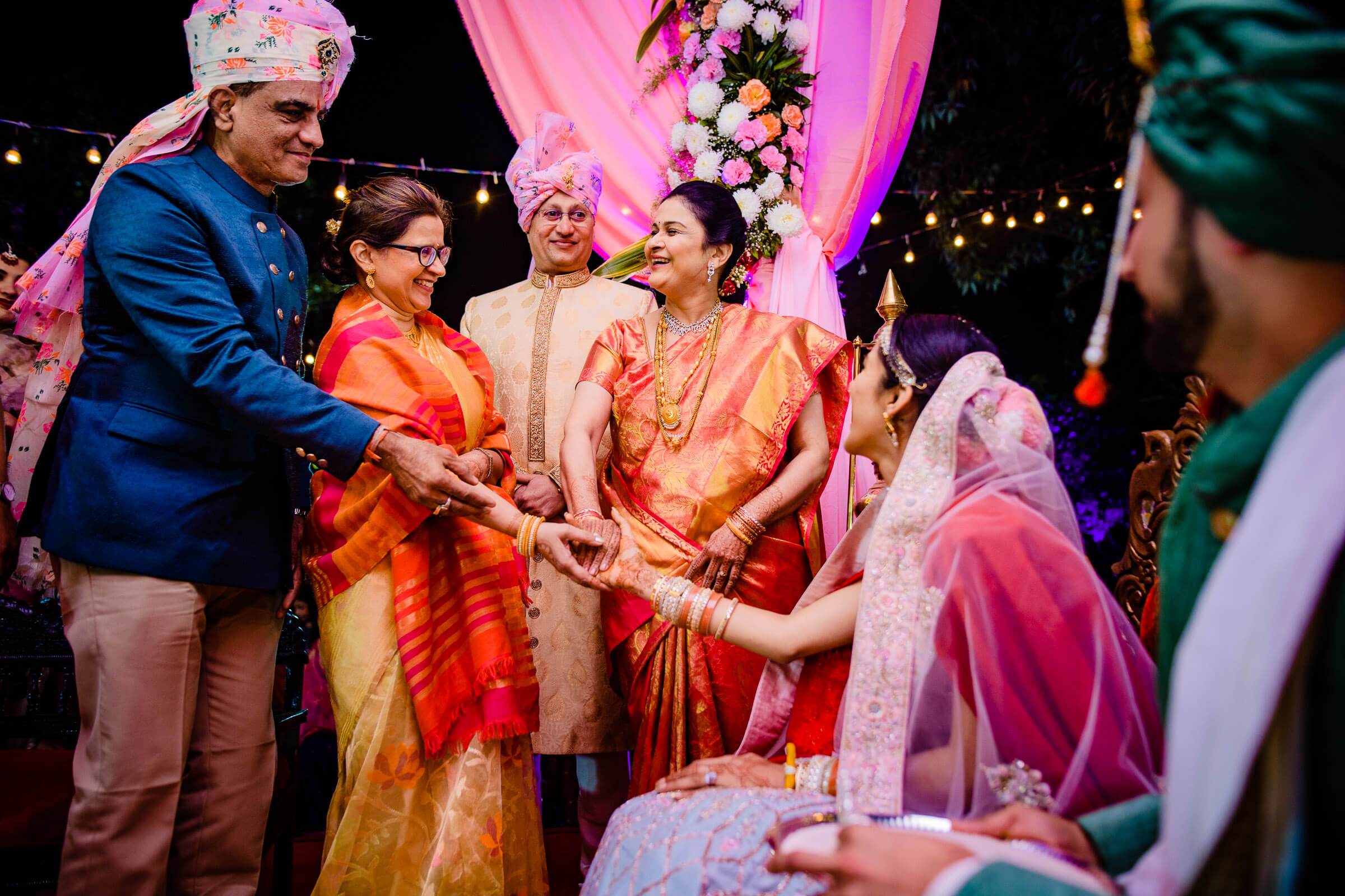 Shreya and Yash greet guests in traditional gold and orange attire under pink-lit floral arch at Mahabaleshwar