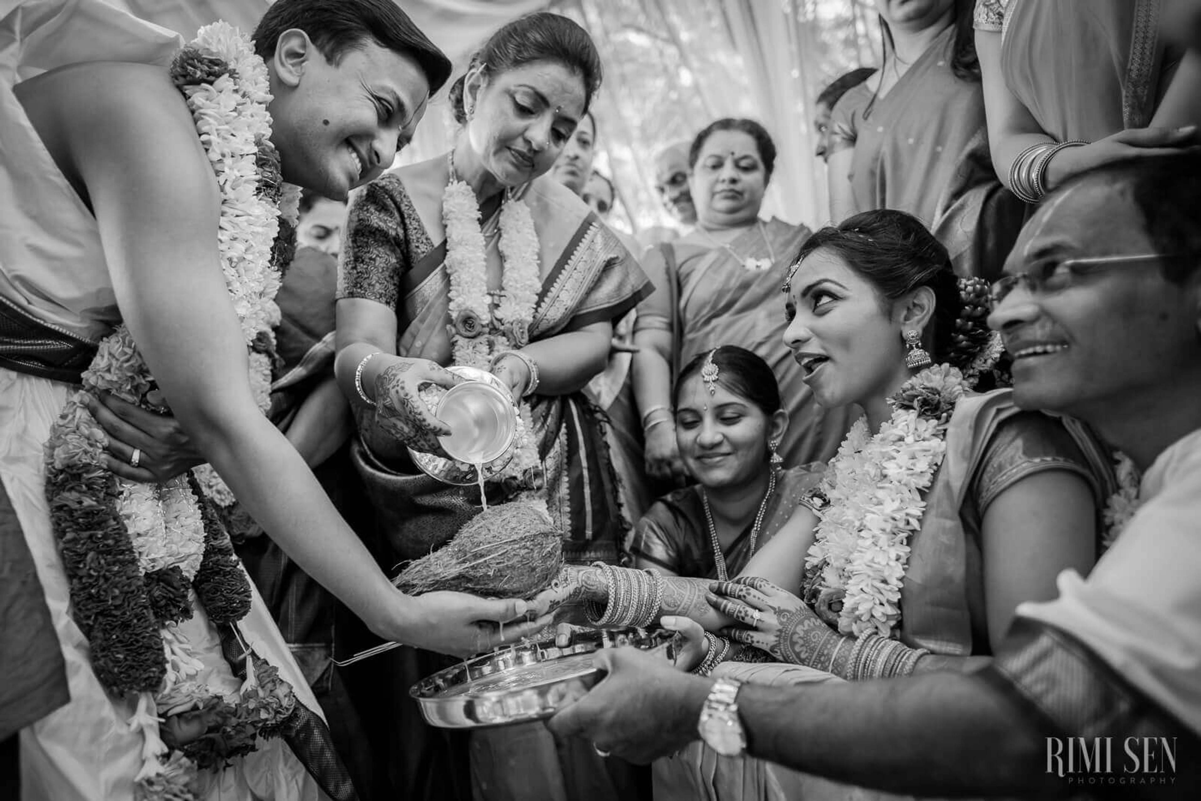 Pooja and Aniket exchange ceremonial offerings surrounded by smiling family members wearing flower garlands in Bangalore