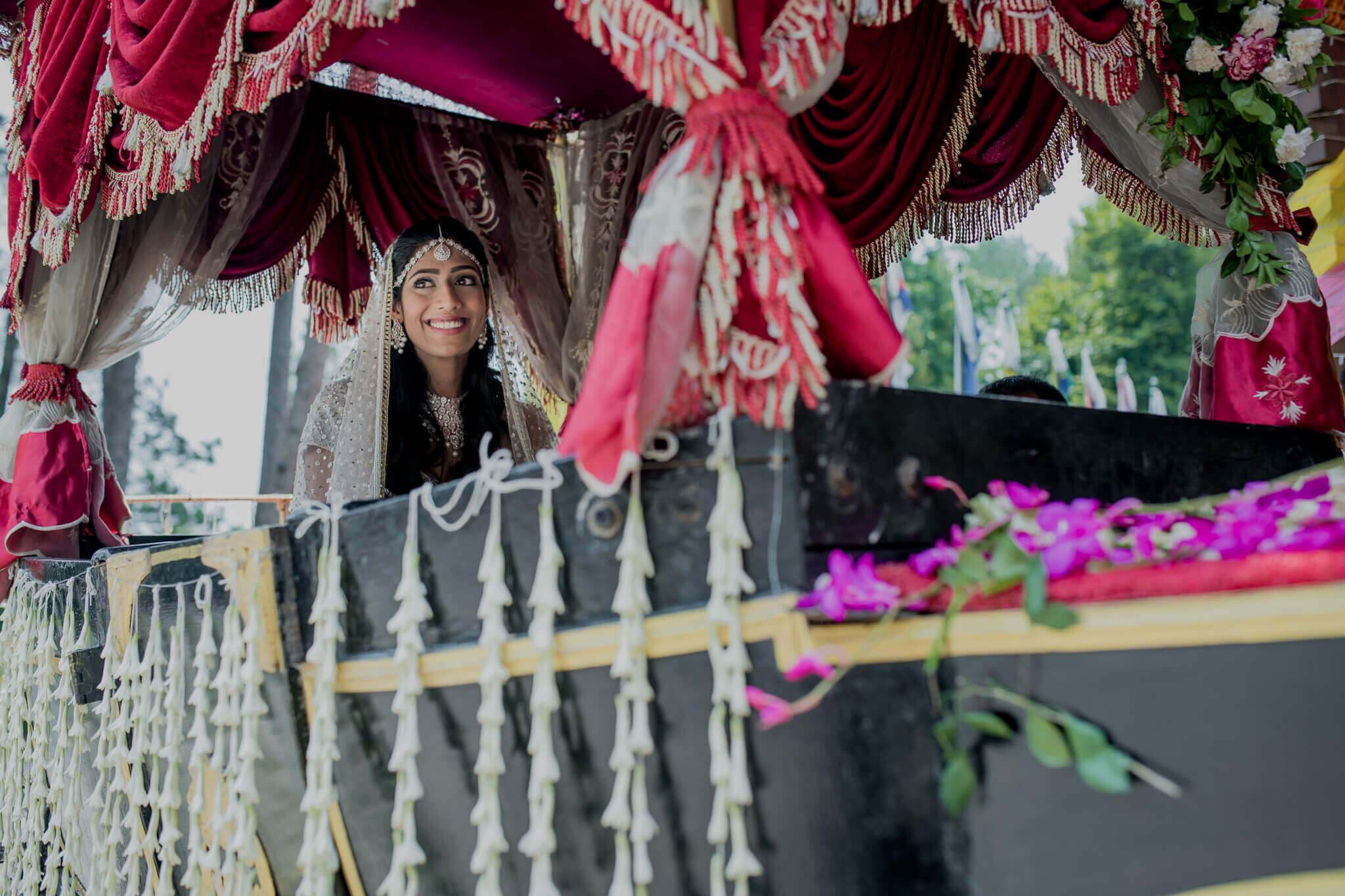 Anu smiles beneath crimson draped fabric and ornate decorations in Nepal, framed by magenta flowers