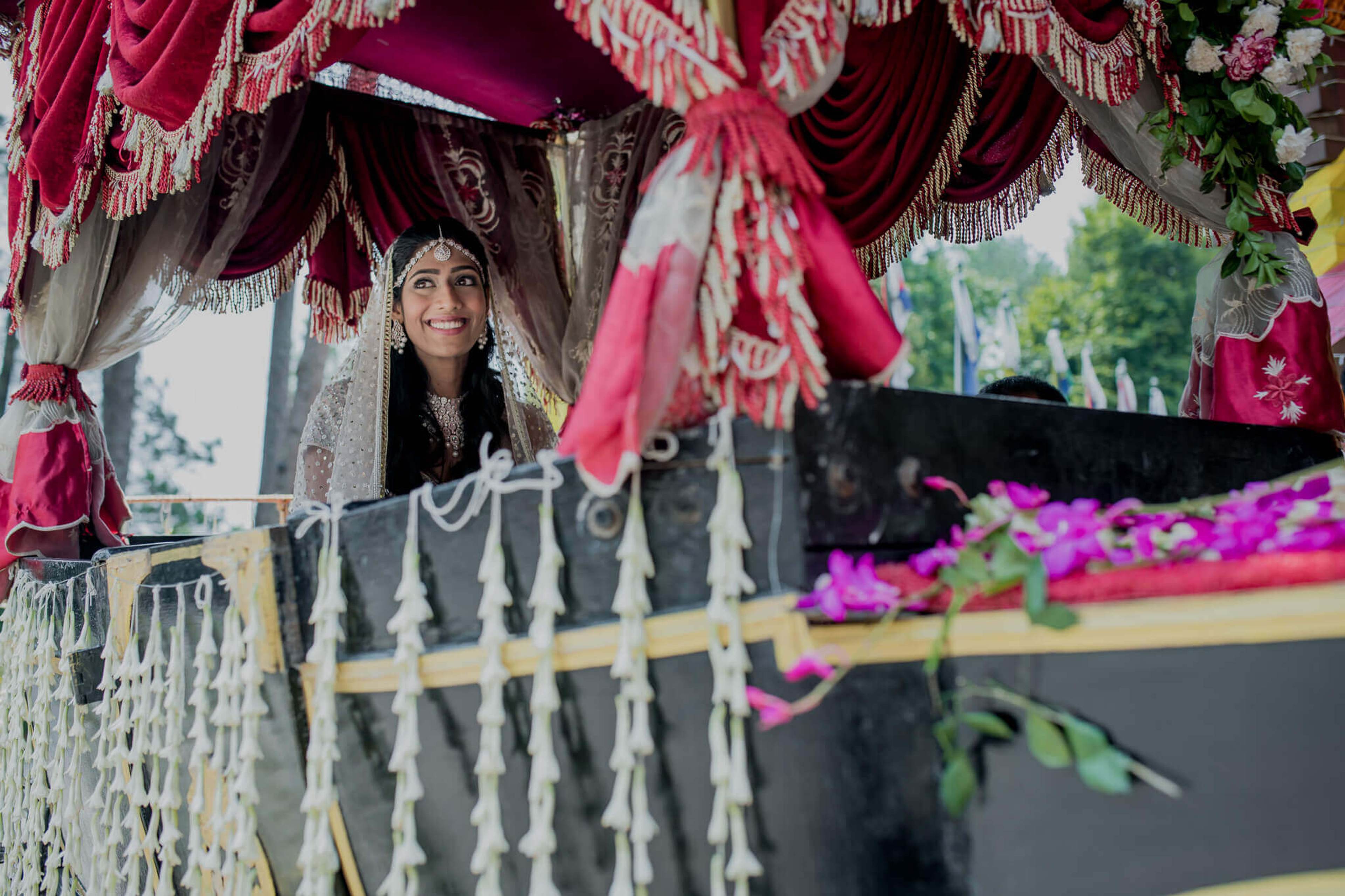 Anu smiles beneath crimson draped fabric and ornate decorations in Nepal, framed by magenta flowers