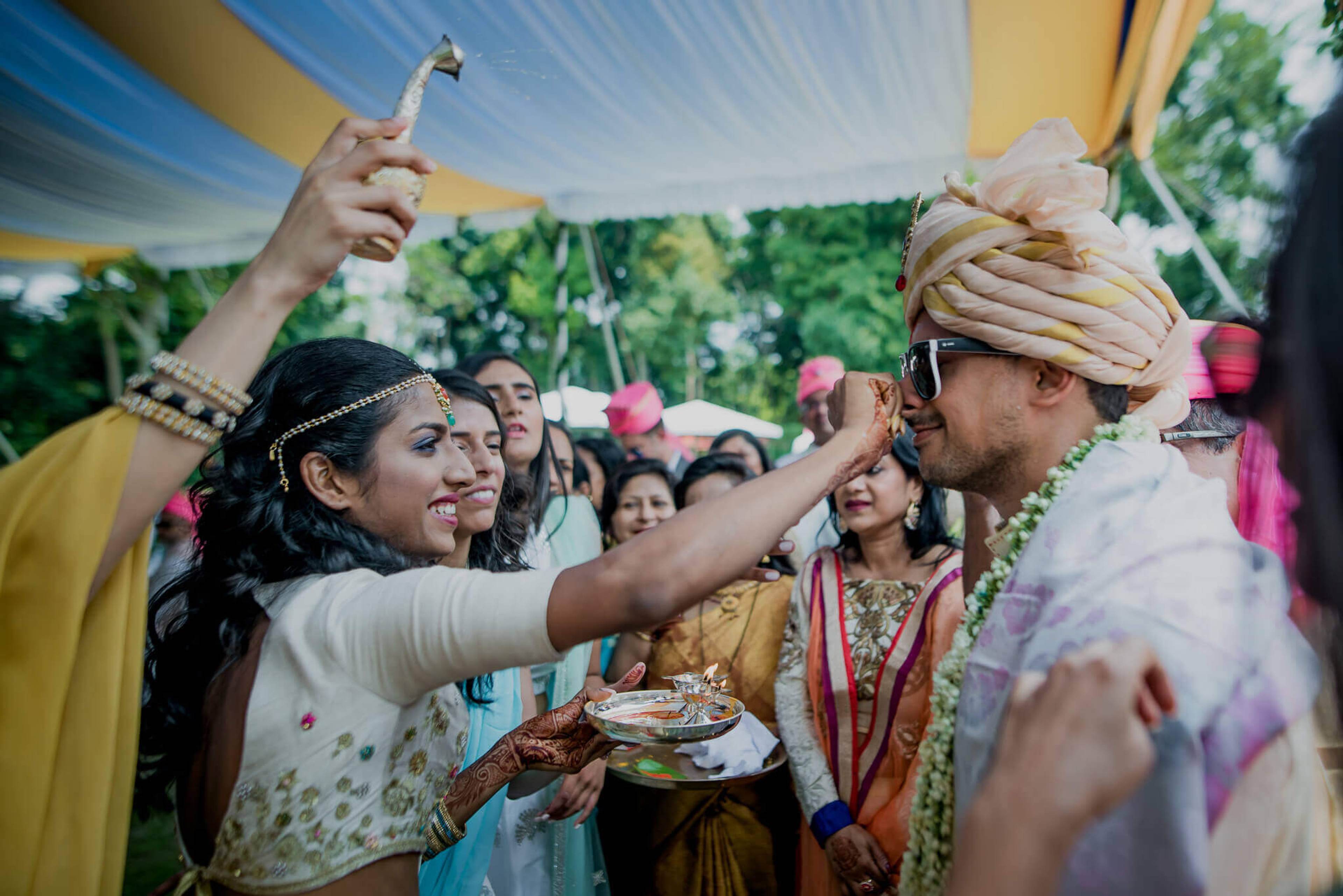 Anu applies vermillion to Raghu's face during colorful wedding festivities in Nepal, surrounded by guests