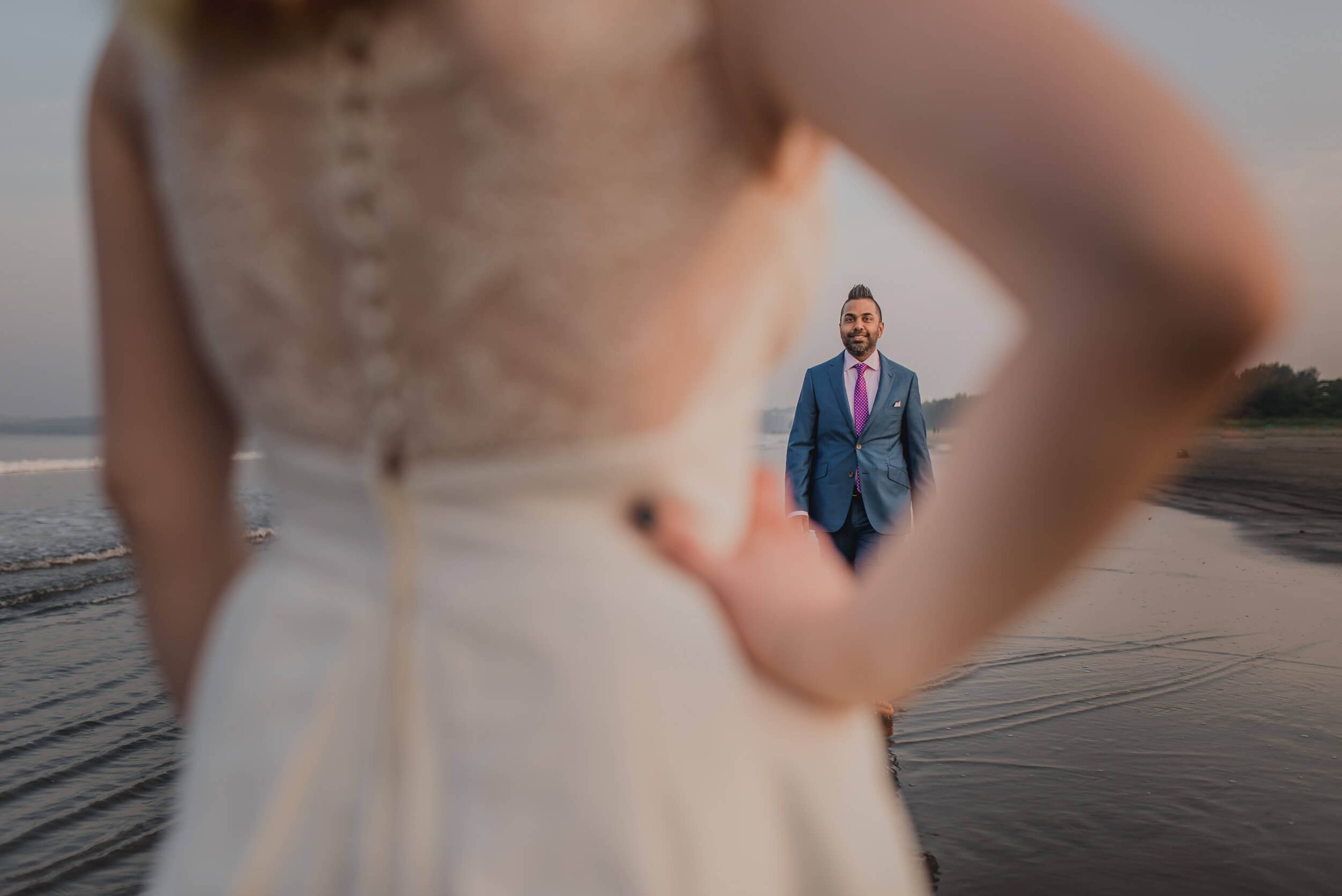 Sarah in beaded gown frames Ravin in navy suit on Goa beach at dusk