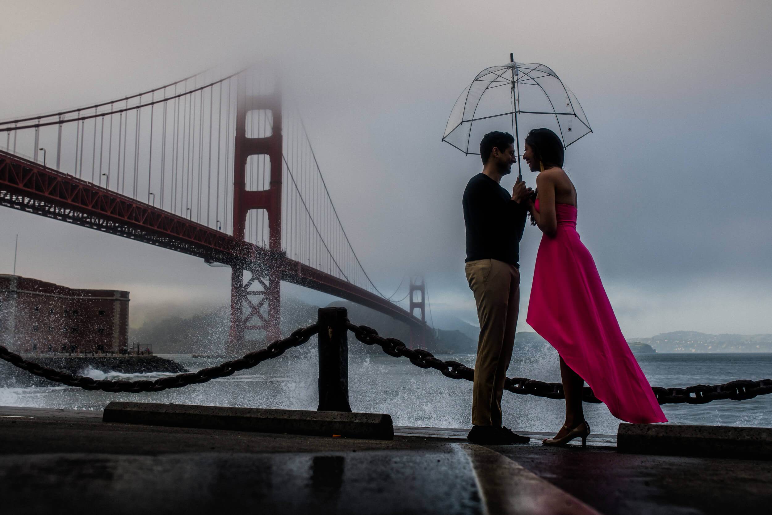 Anu and Raghu kiss under umbrella by Golden Gate Bridge in misty California light