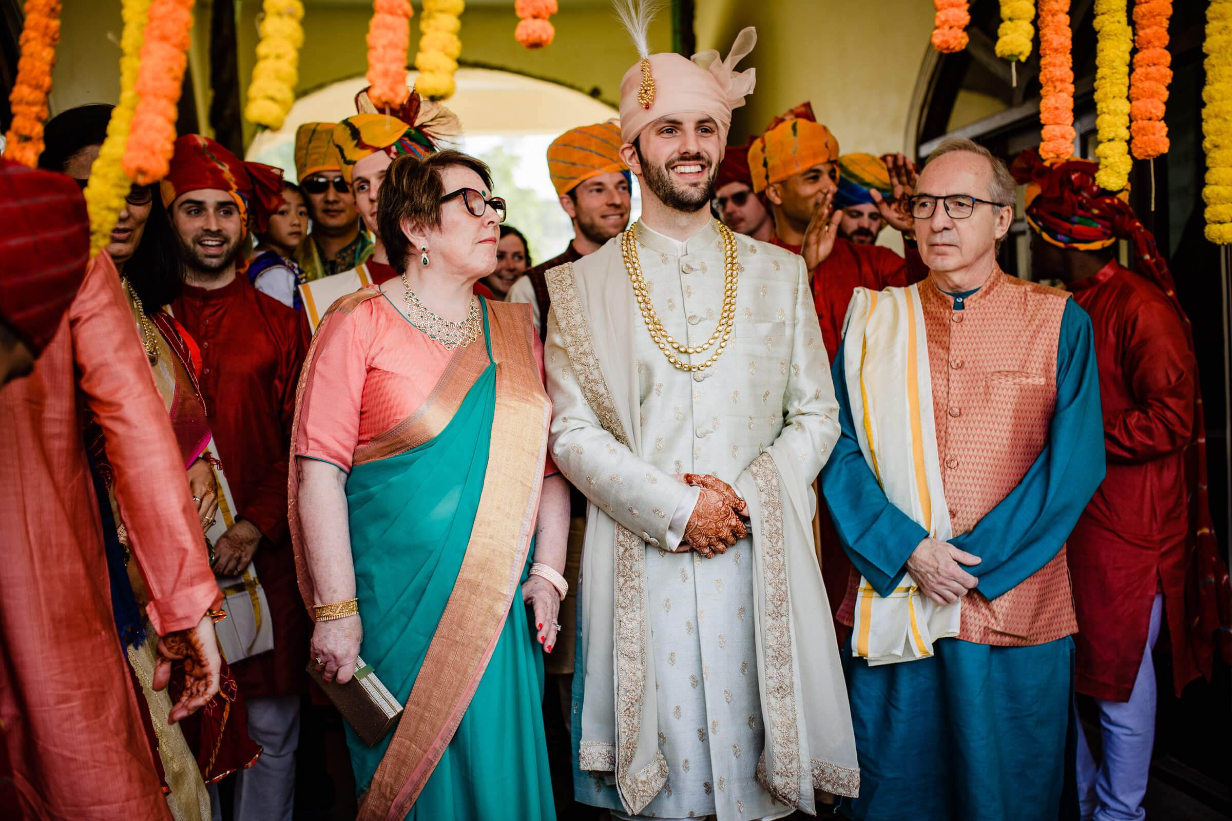 Maitrayee and Eric in traditional wedding attire surrounded by guests wearing colorful turbans and traditional Indian clothing at their Rajasthan celebration