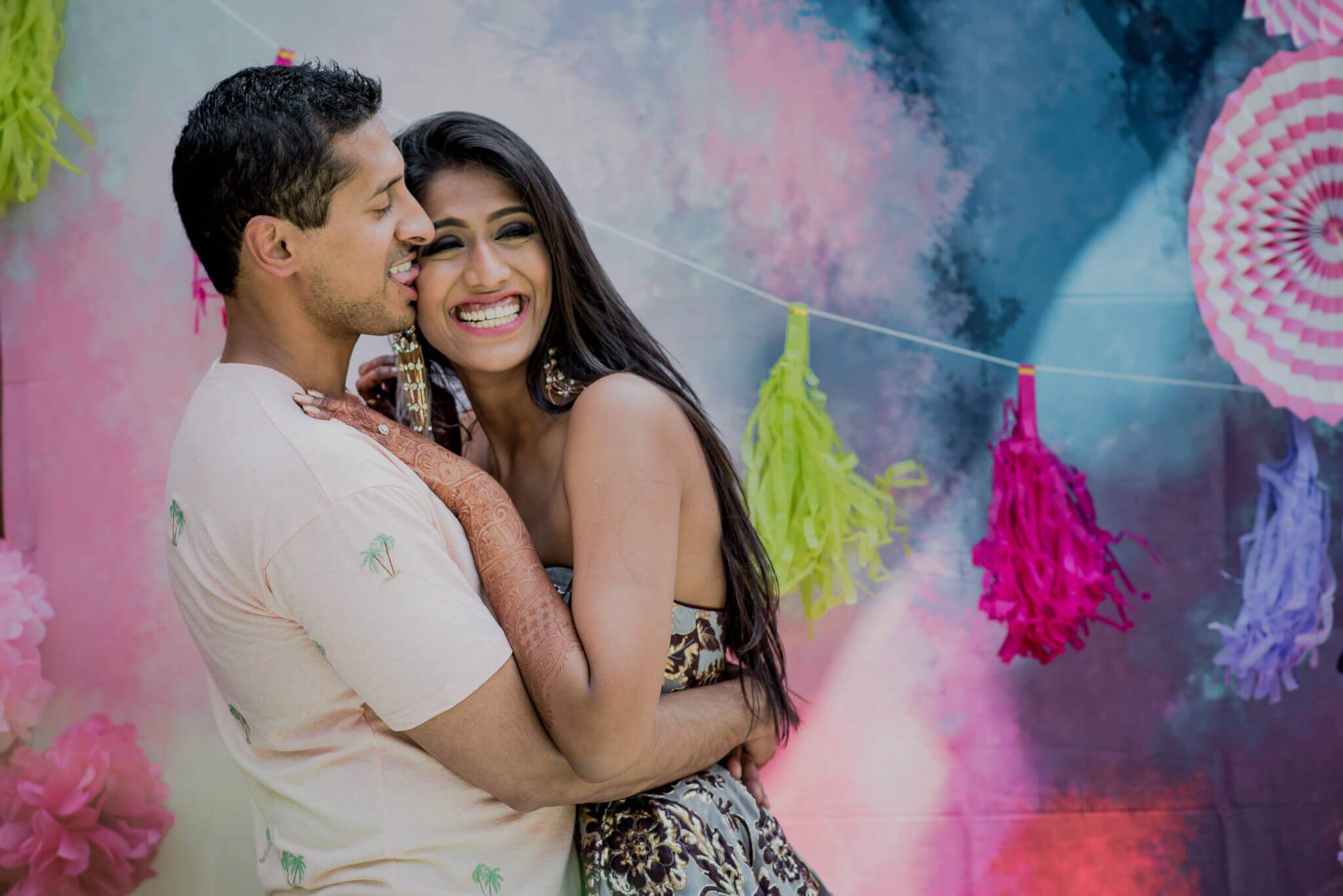 Anu and Raghu embrace and smile amid colorful paper fan backdrop and hanging tassels in Nepal
