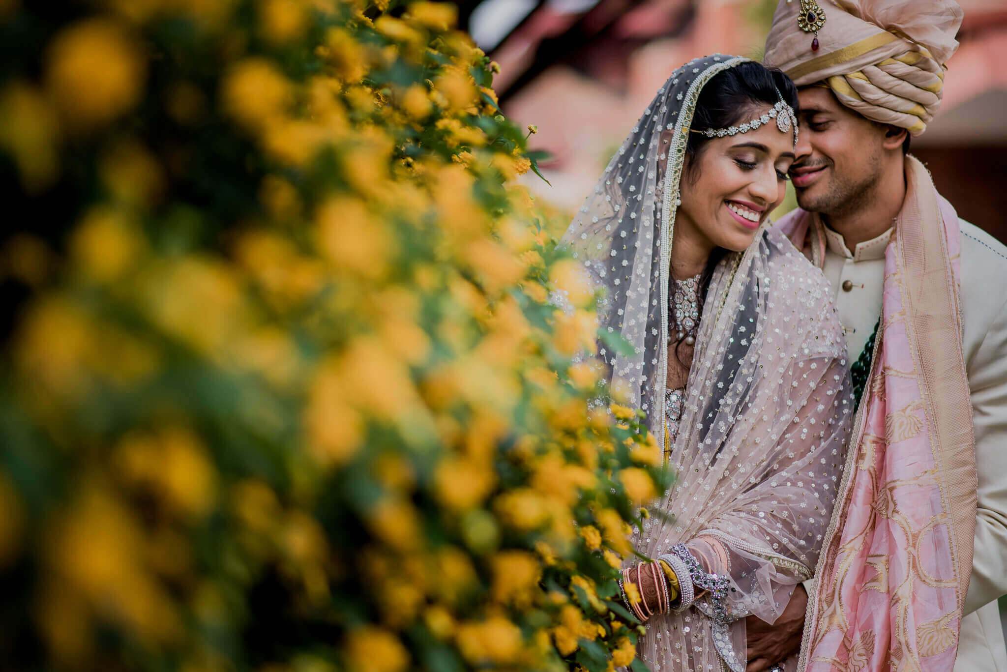 Anu and Raghu share an intimate moment framed by yellow flowers in traditional wedding attire