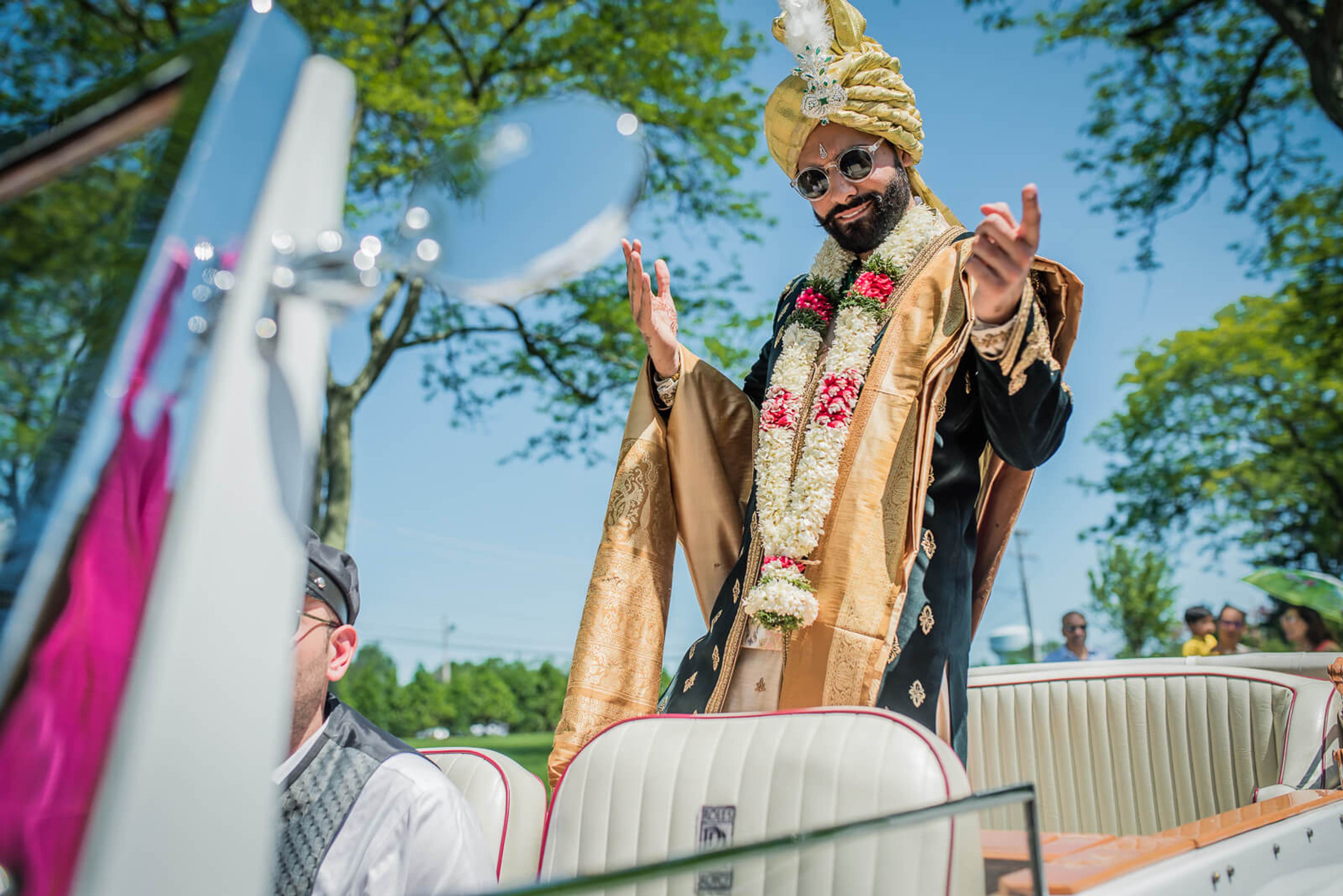 Ankit in gold ceremonial attire and floral garland, greeting guests outdoors under trees in New York