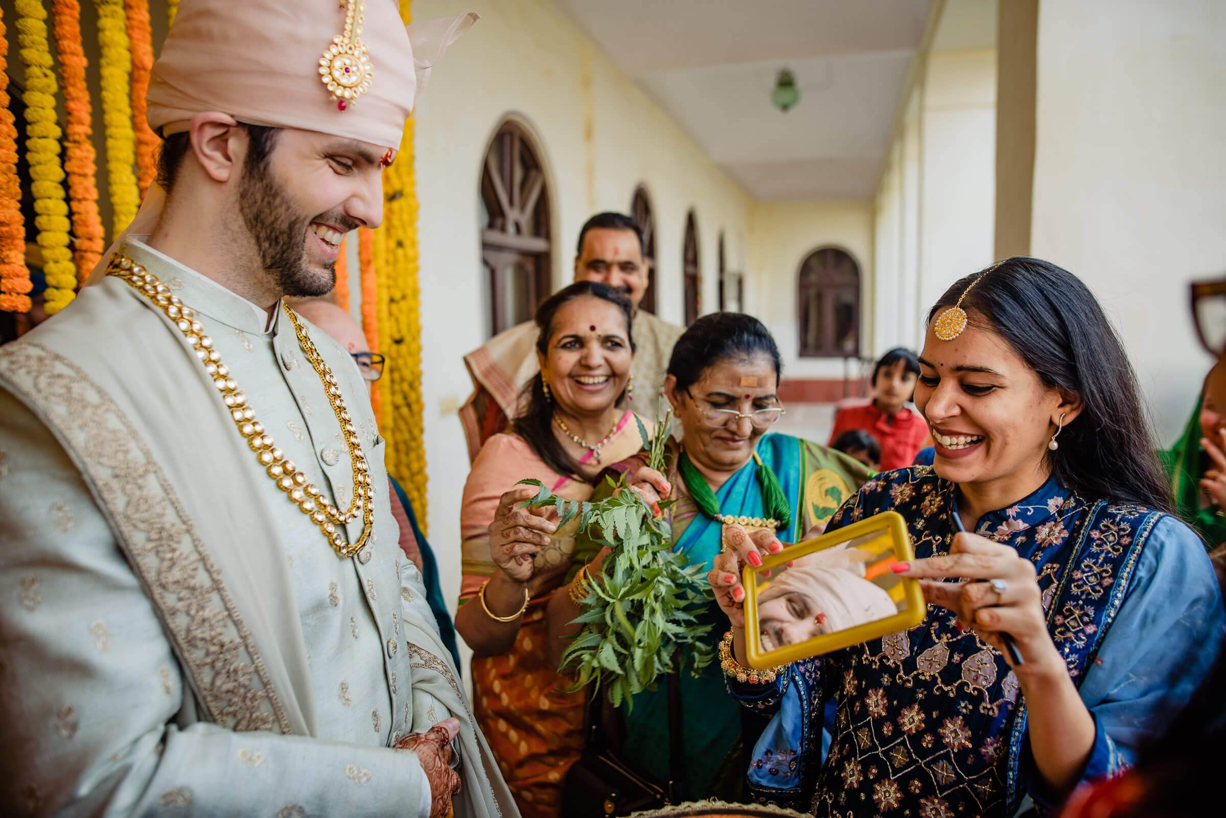 Groom Eric in traditional white sherwani and turban laughing with family holding gifts in Rajasthan